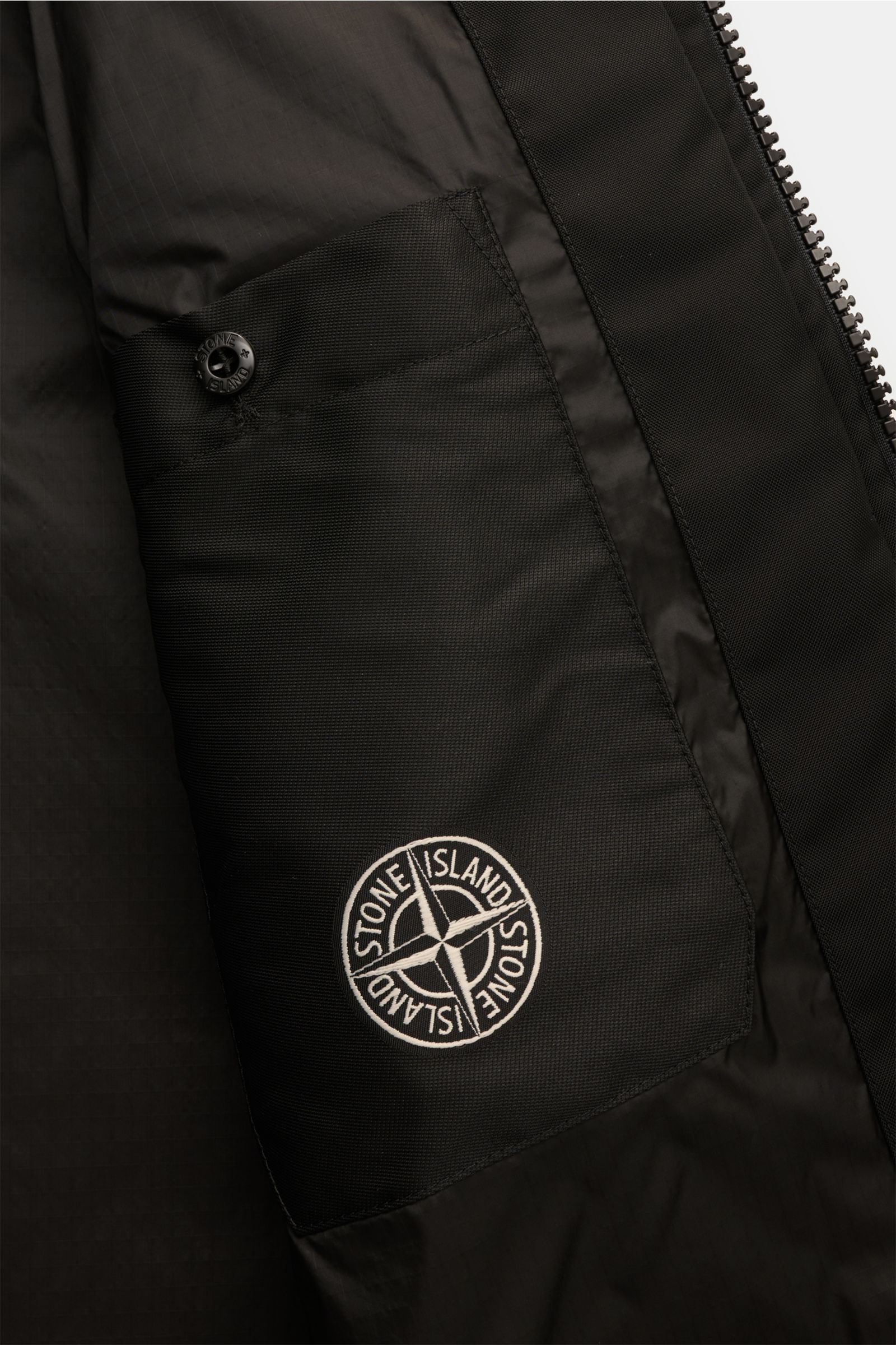 Close-up interior view of Stone Island Jacket 'Panno Ratinato' black showing logo patch on inside pocket with button closure and zip detail.

Functional and eye-catching: This STONE ISLAND hooded jacket is an eye-catching, sporty piece for the colder m
