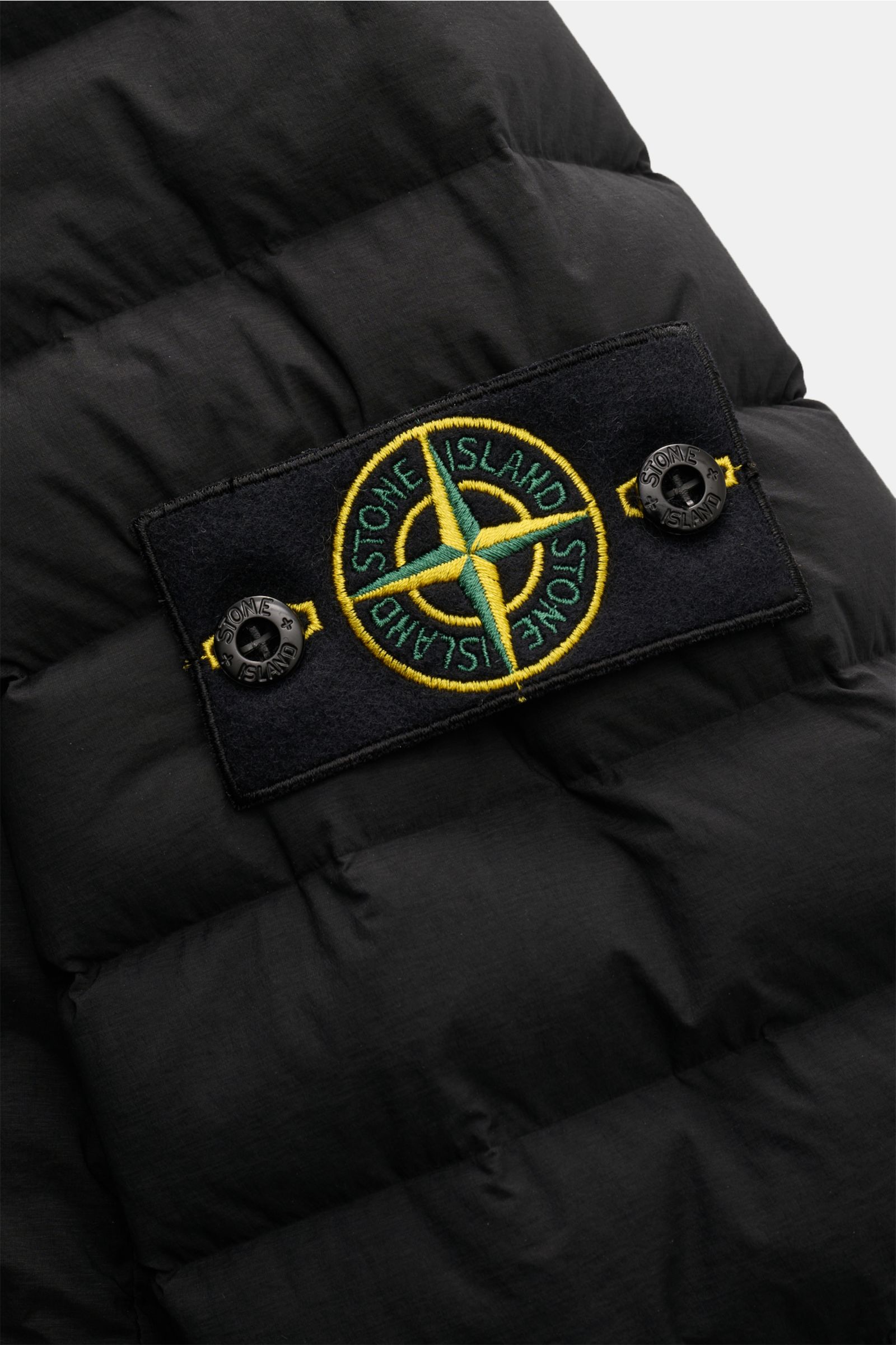 Nahaufnahme des typischen Kompass-Badges an der schwarzen Stone Island Daunenjacke 'Seamless Tunnel Nylon Down-TC' aus hochwertiger Microfaser mit leichter Daunenfüllung.