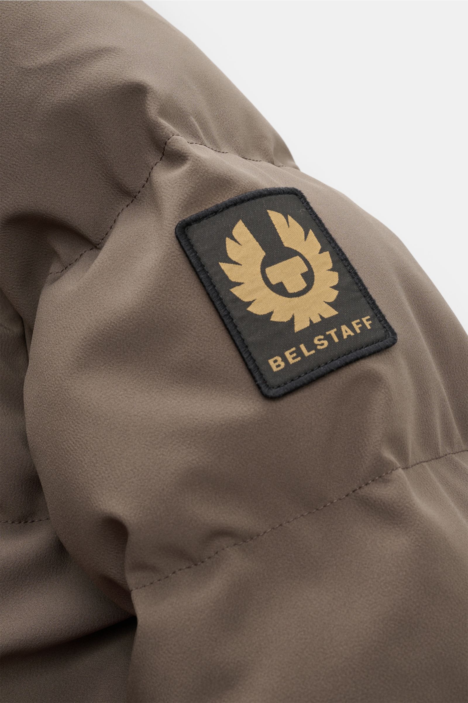 Nahaufnahme der Belstaff Daunenjacke 'Pendulum' graugrün am Oberarm mit dem schwarzen BELSTAFF-Label, hochwertige Microfaser, wind- und wasserabweisend.