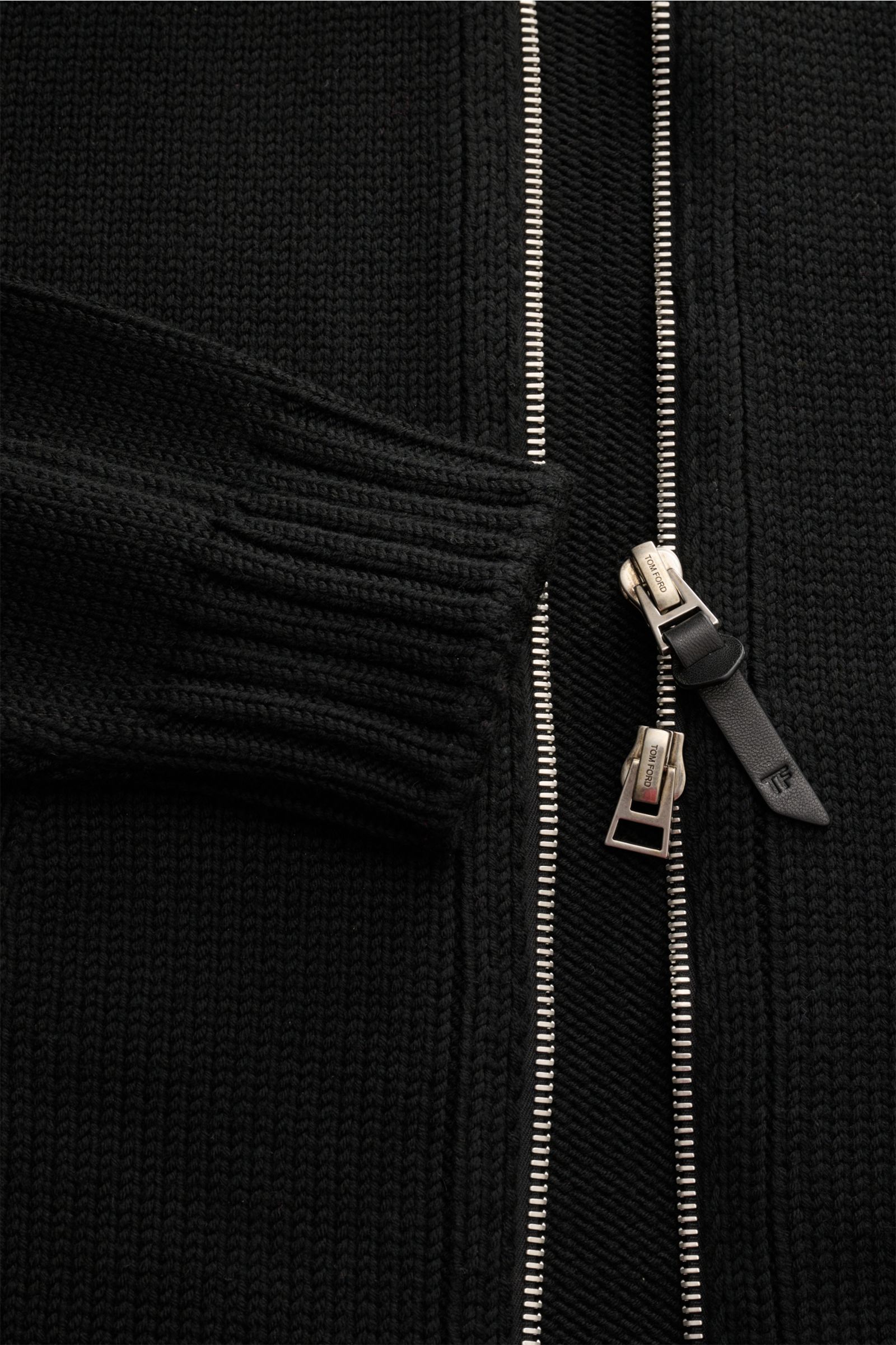 Close-up front view of a black knitted jacket with silver two-way zipper and ribbed cuff, highlighting detailed texture and zipper pull; Tom Ford Velourslederjacke hellbraun. Luxus in seiner lässigsten Form erwartet Sie bei TOM FORD mit diesem typische
