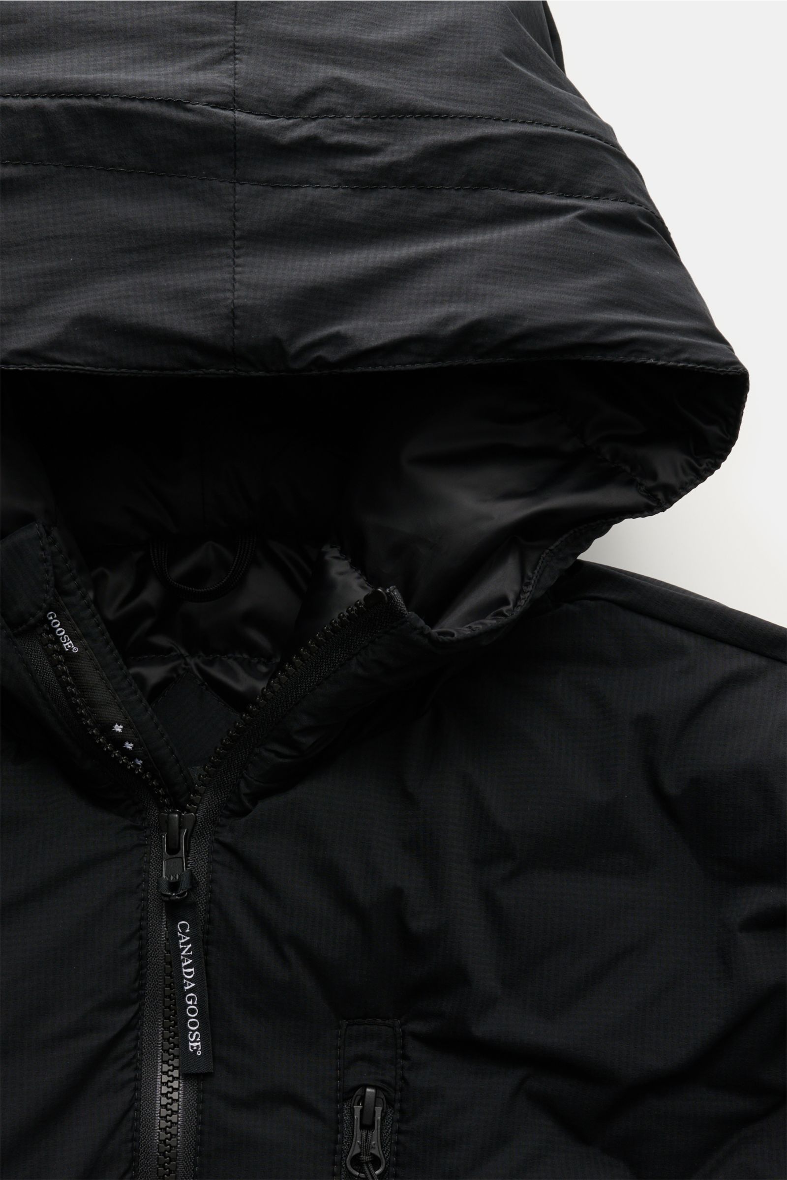 Nahaufnahme der Kapuze und des oberen Bereichs der Canada Goose Daunenjacke 'Lodge Hoody' schwarz aus Ripstop-Microfaser mit Reißverschluss.