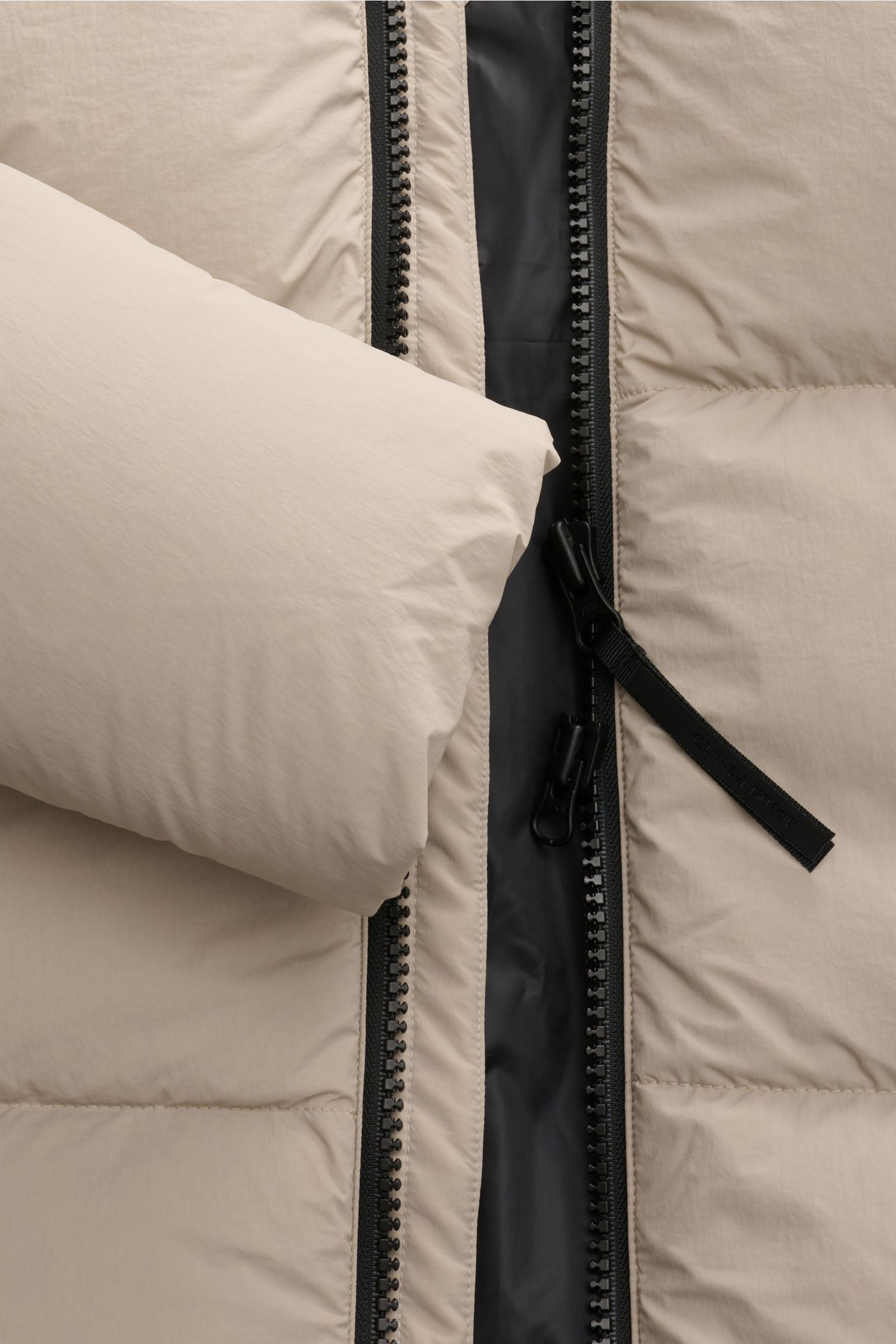 Nahaufnahme der Canada Goose Daunenjacke 'Crofton Puffer' sand aus der Frontperspektive mit offenem Zwei-Wege-Reißverschluss, voluminöser Daunenfüllung und glattem Innenfutter.