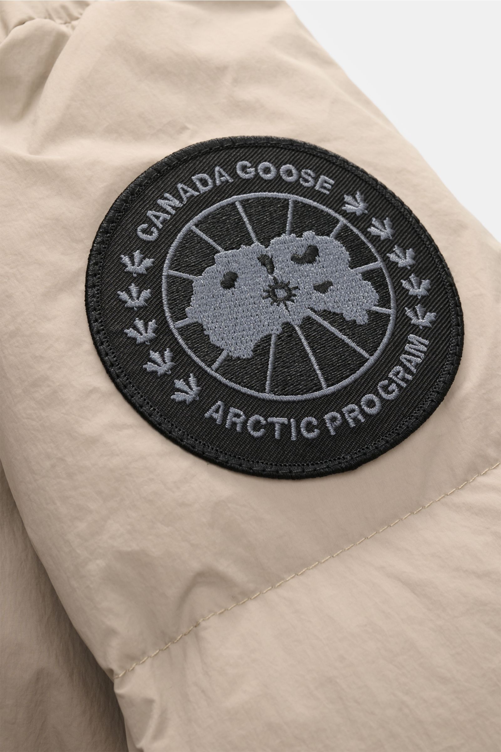 Nahaufnahme des tonalen Canada Goose Logos auf der linken Ärmelseite der sandfarbenen Canada Goose Daunenjacke 'Crofton Puffer' aus Microfaser.