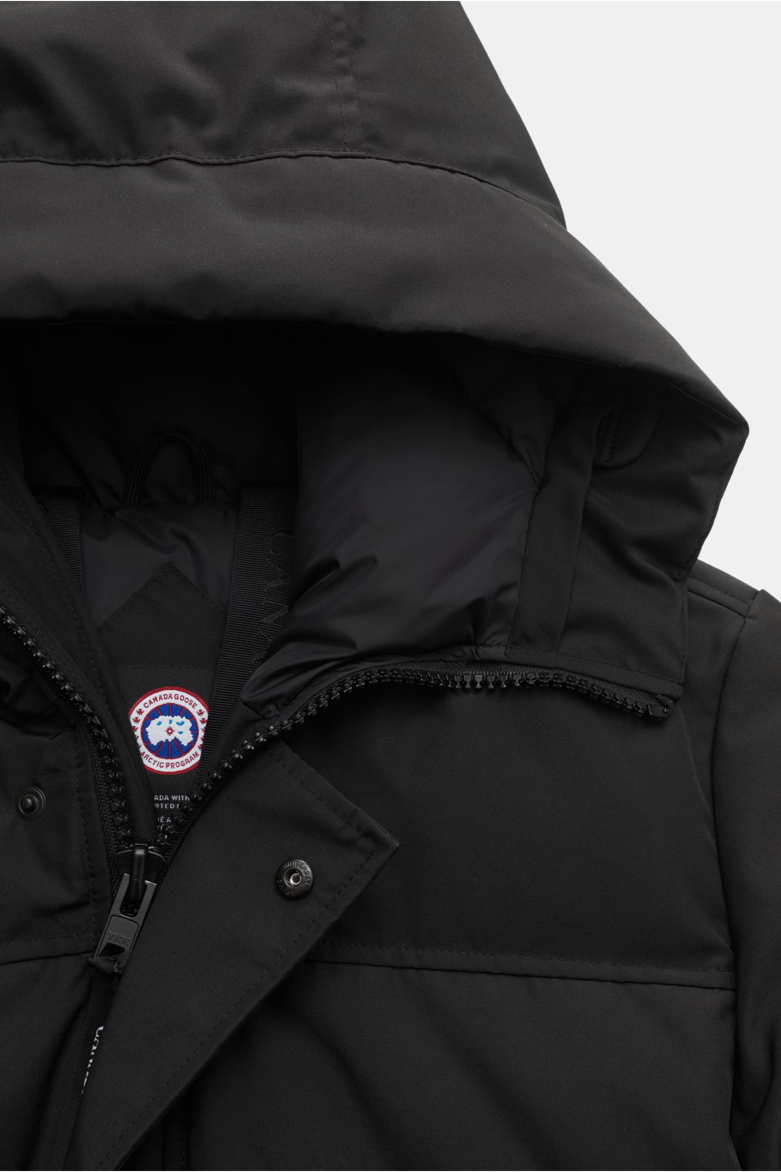 Canada Goose Daunenjacke 'Macmillan' schwarz, Nahaufnahme von oben, mit hochschließender Kapuze, Reißverschluss, Druckknöpfen und innenliegenden Rucksack-Riemen.