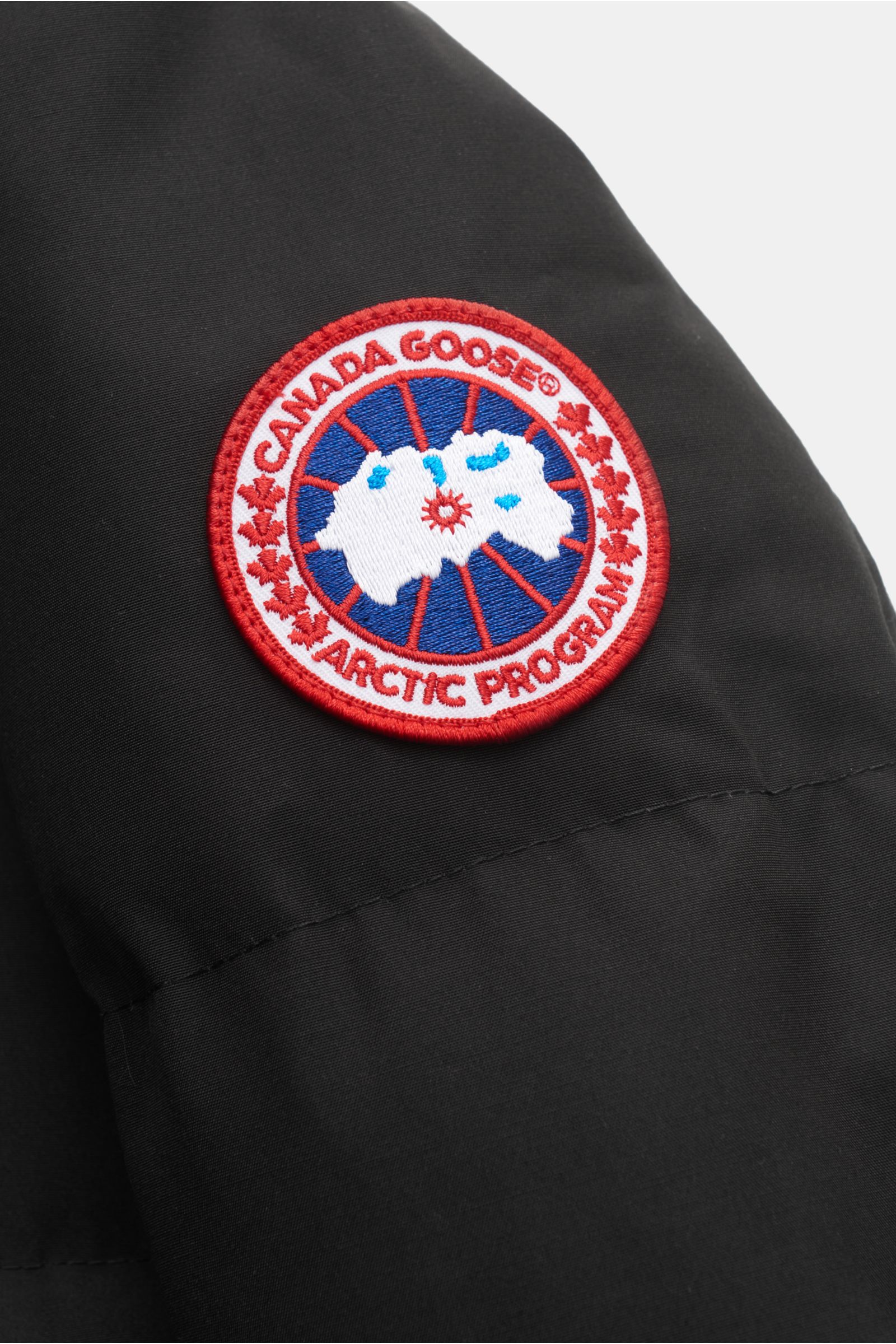 Canada Goose Daunenjacke 'Macmillan' schwarz, Nahaufnahme Schulter mit rotem Logo, wasserabweisend, Slim Fit, Daunenfüllung, Kapuze, Rucksackriemen innen.