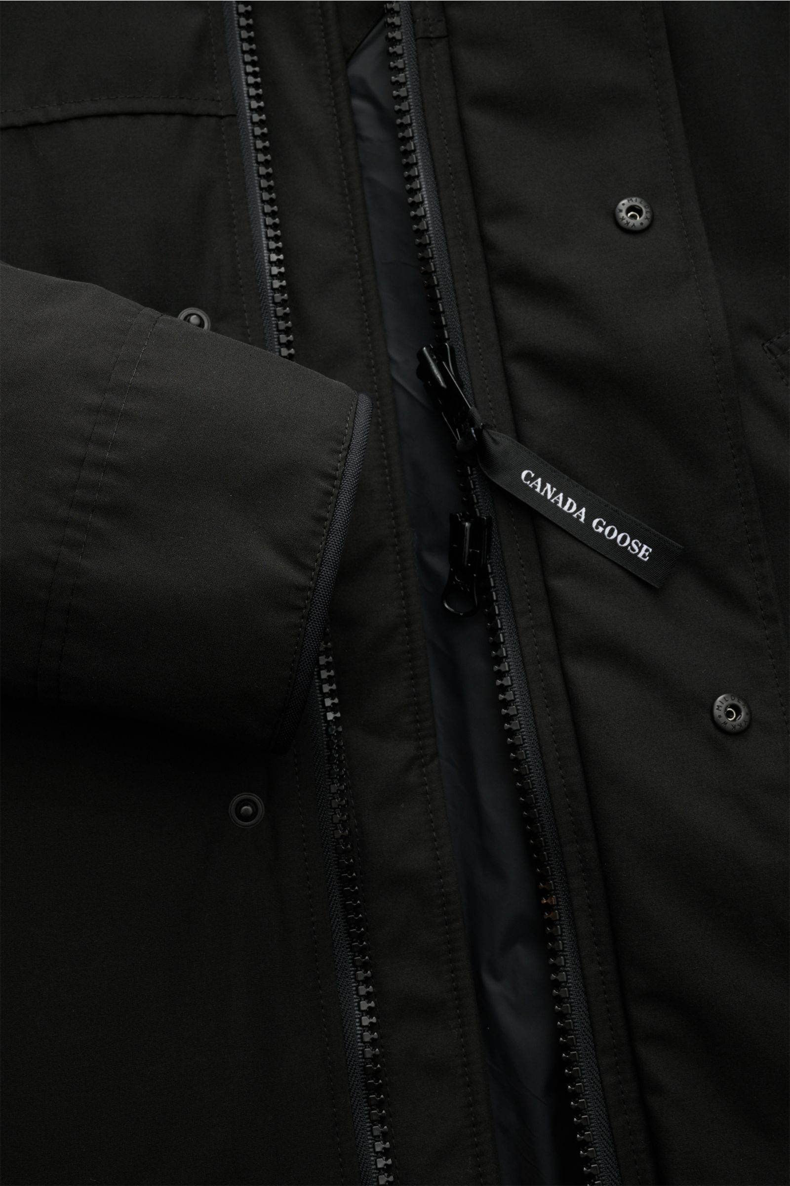 Nahaufnahme aus schräger Perspektive des schwarzen Canada Goose Daunenparka 'Langford' mit Arctic-Tech-Material, Daunenfüllung, Reißverschluss und Druckknöpfen.