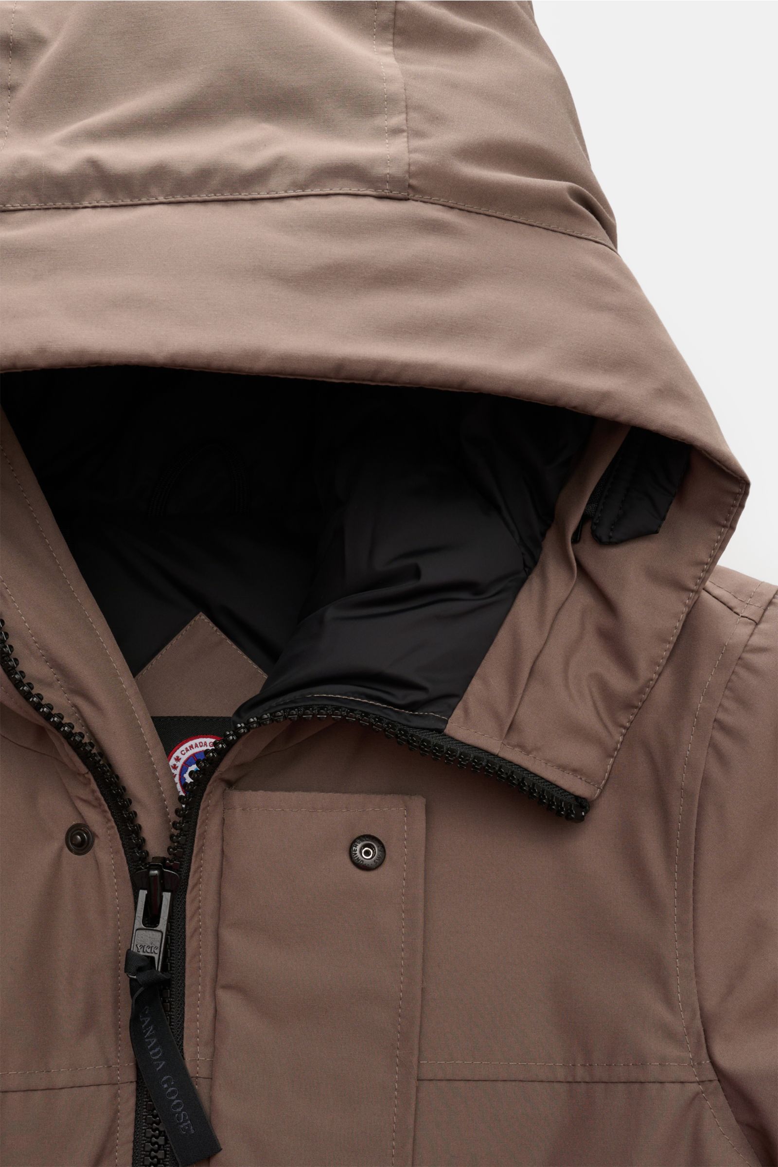 Nahaufnahme aus schräger Frontalperspektive des Canada Goose Daunenparka 'Langford' taupe mit Arctic-Tech-Material, wärmender Daunenfüllung, Kapuze, Zwei-Wege-Reißverschluss und Windblende mit Druckknöpfen.