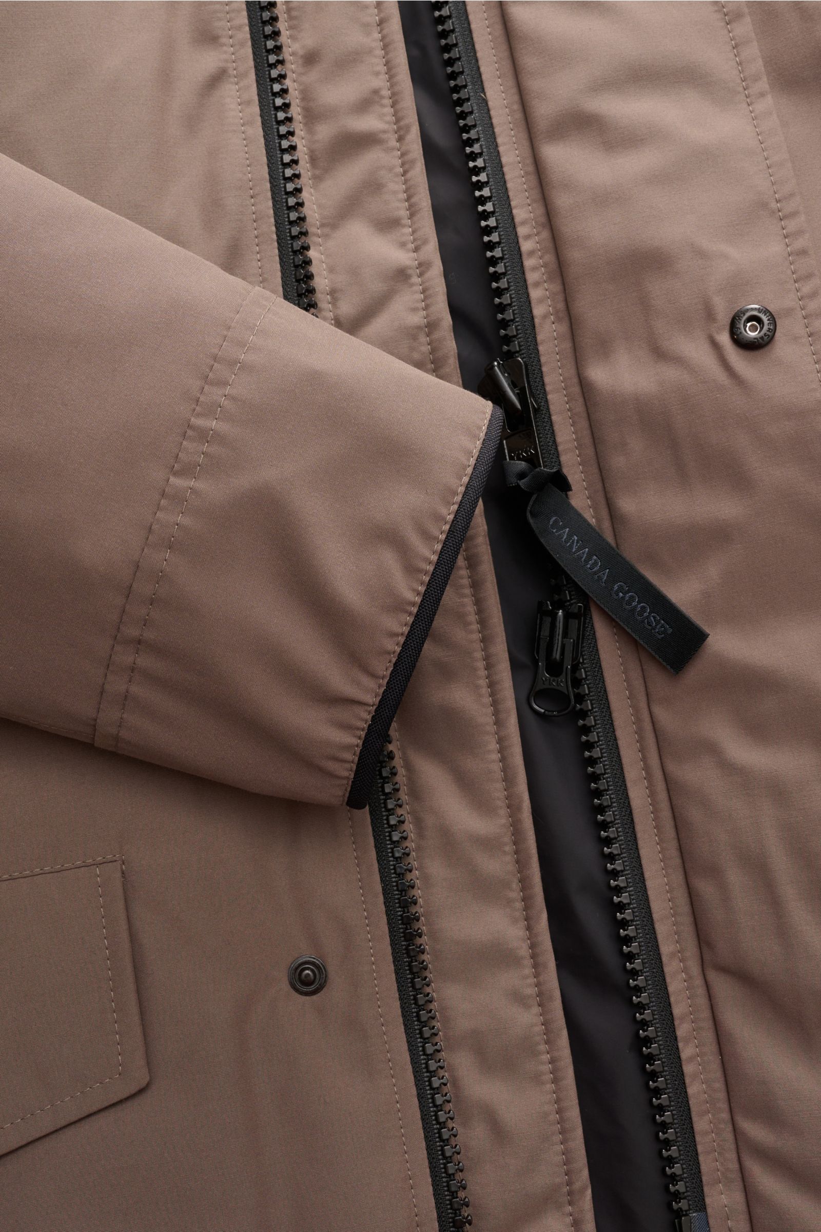 Nahaufnahme des Canada Goose Daunenparka 'Langford' taupe von vorne, zeigt Reißverschluss, Druckknöpfe, Ärmel und Material mit Arctic-Tech.