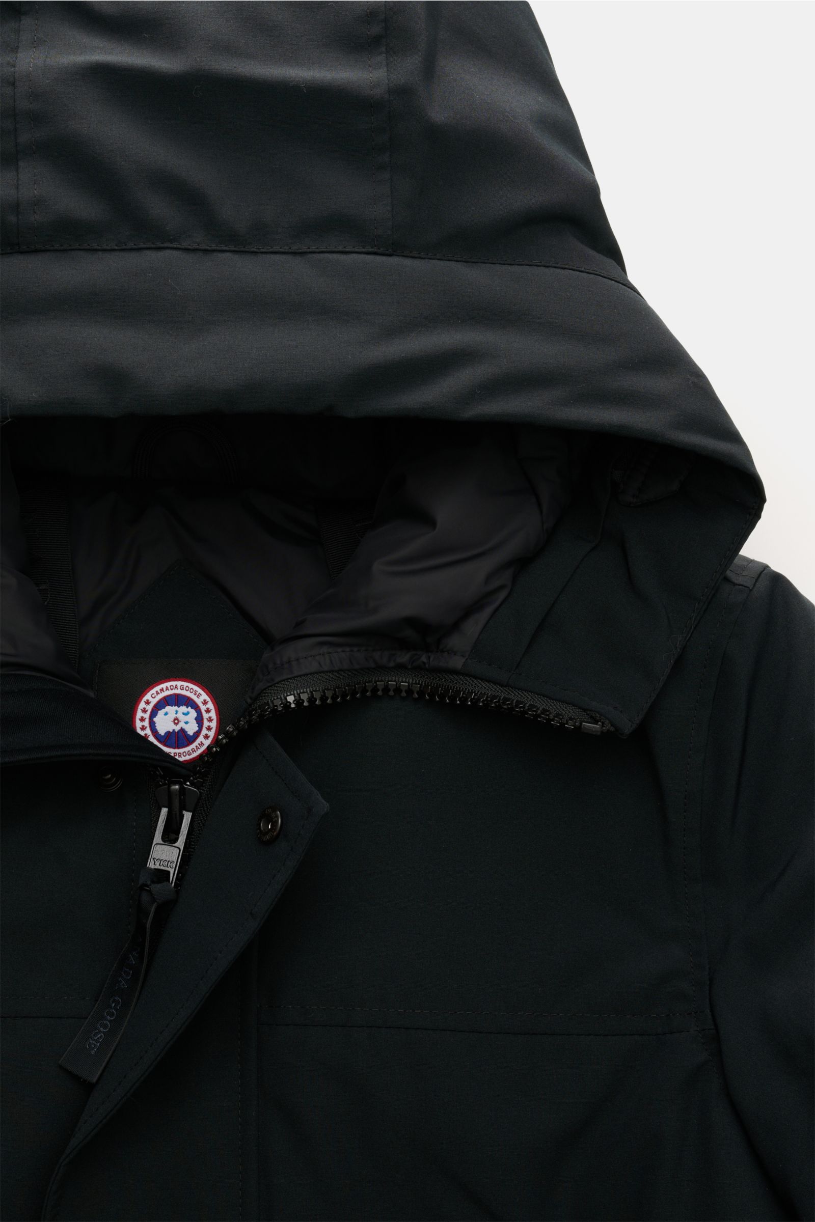 Close-up front view of Canada Goose Down parka 'Langford' black, showing hood, zipper, snap buttons, and the logo inside the collar. Urban style with an arctic background – the down parka 'Langford' by CANADA GOOSE impresses with its clear, functional des