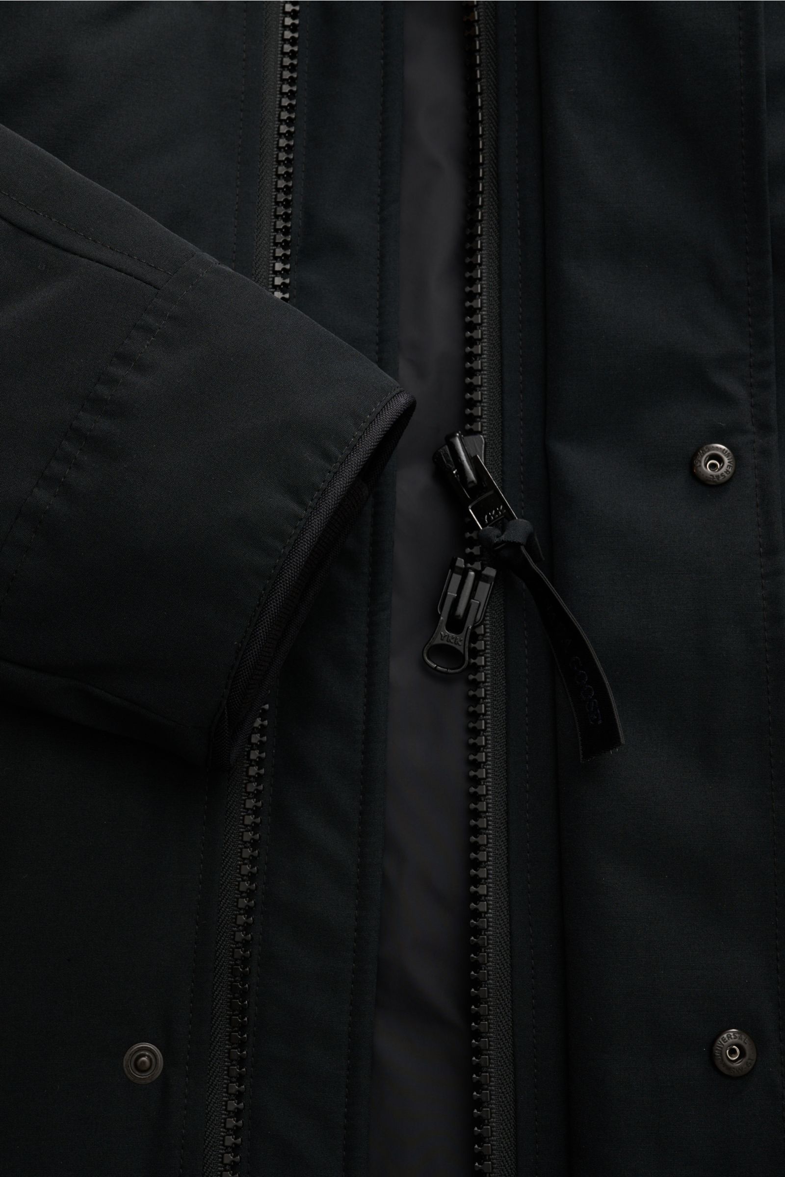 Close-up front view of the Canada Goose Down parka 'Langford' black showing the two-way zipper, storm flap with snap buttons, and sleeve cuff. Urban style with an arctic background – the down parka 'Langford' by CANADA GOOSE impresses with its clear, func