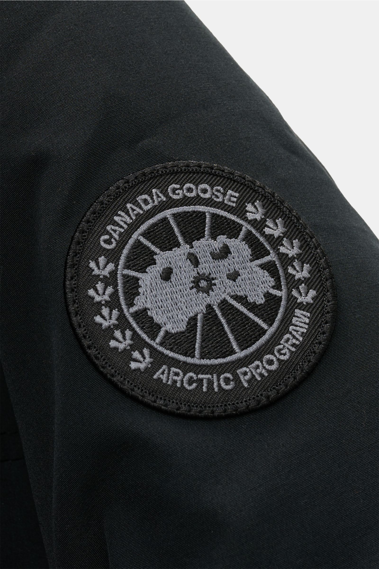 Close-up of the tonal woven label on the upper sleeve of the Canada Goose Down parka 'Langford' black, photographed from the side. Urban style with an arctic background – the down parka 'Langford' by CANADA GOOSE impresses with its clear, functional desig