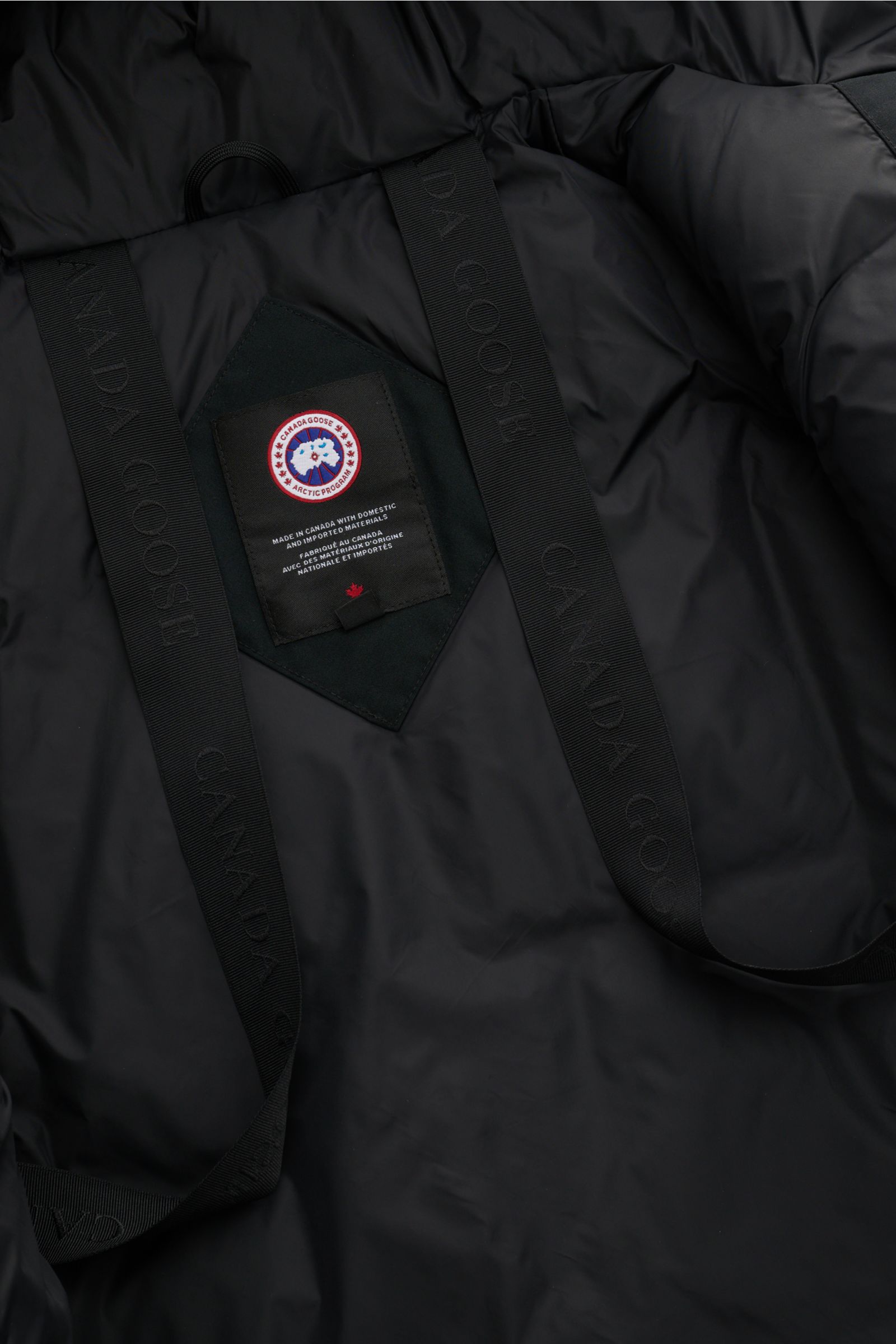 Close-up interior view of Canada Goose Down parka 'Langford' black, showing Arctic-Tech material, label, and internal rucksack straps. Urban style with an arctic background – the down parka 'Langford' by CANADA GOOSE impresses with its clear, functional d