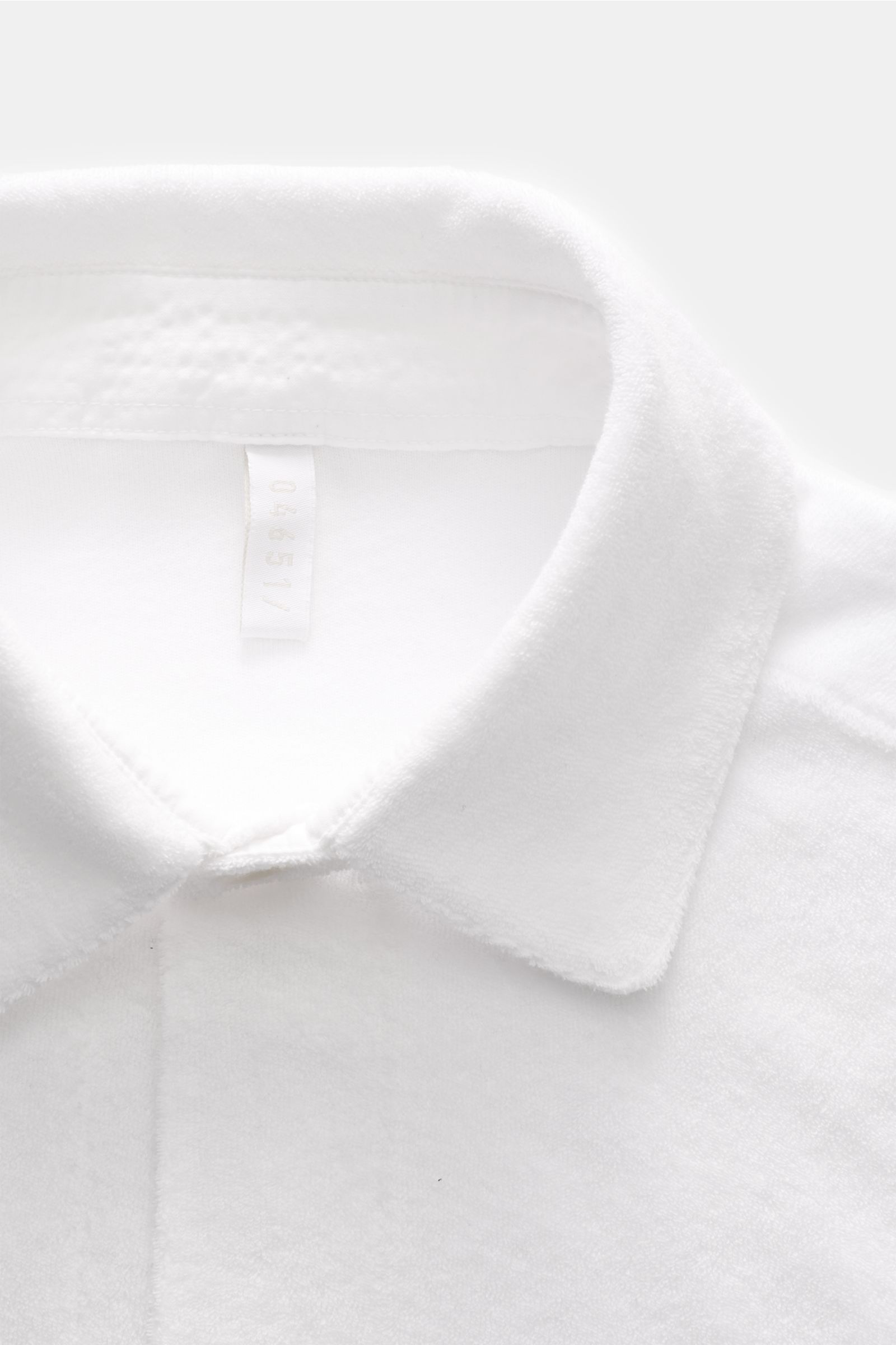 White close-up image of the collar and neckline area of the 04651/ A trip in a bag Frottee-Overshirt 'Terry Jacket' oliv, photographed from above, showing soft cotton terry fabric and fine stitching. Das Overshirt 'Terry Jacket' von 04651/ A TRIP IN A 