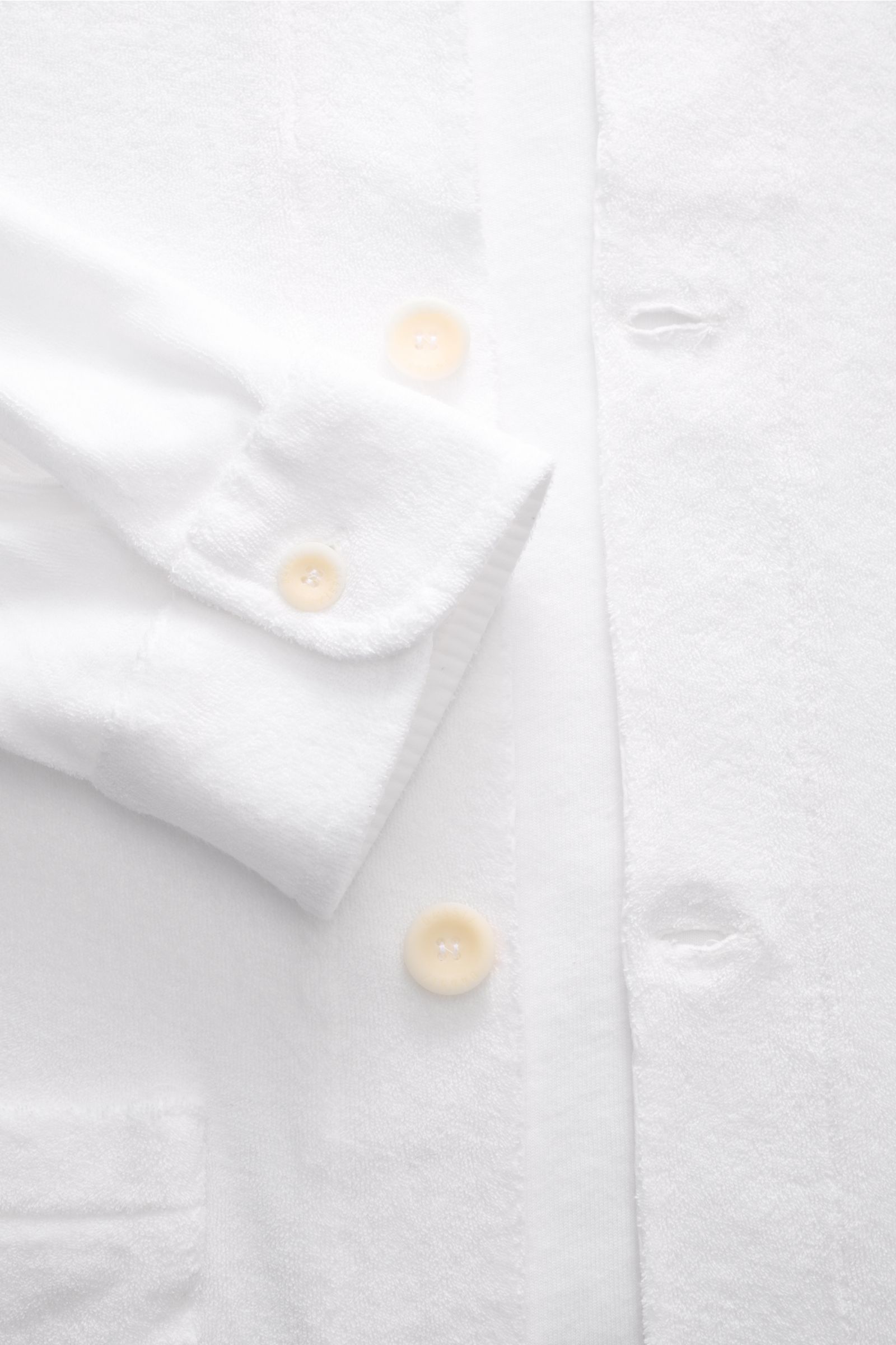 Close-up front view of the 04651/ A trip in a bag Frottee-Overshirt 'Terry Jacket' oliv in white, showing soft cotton terry fabric with beige buttons, a cuff with button, and buttonholes. Das Overshirt 'Terry Jacket' von 04651/ A TRIP IN A BAG bringt mari