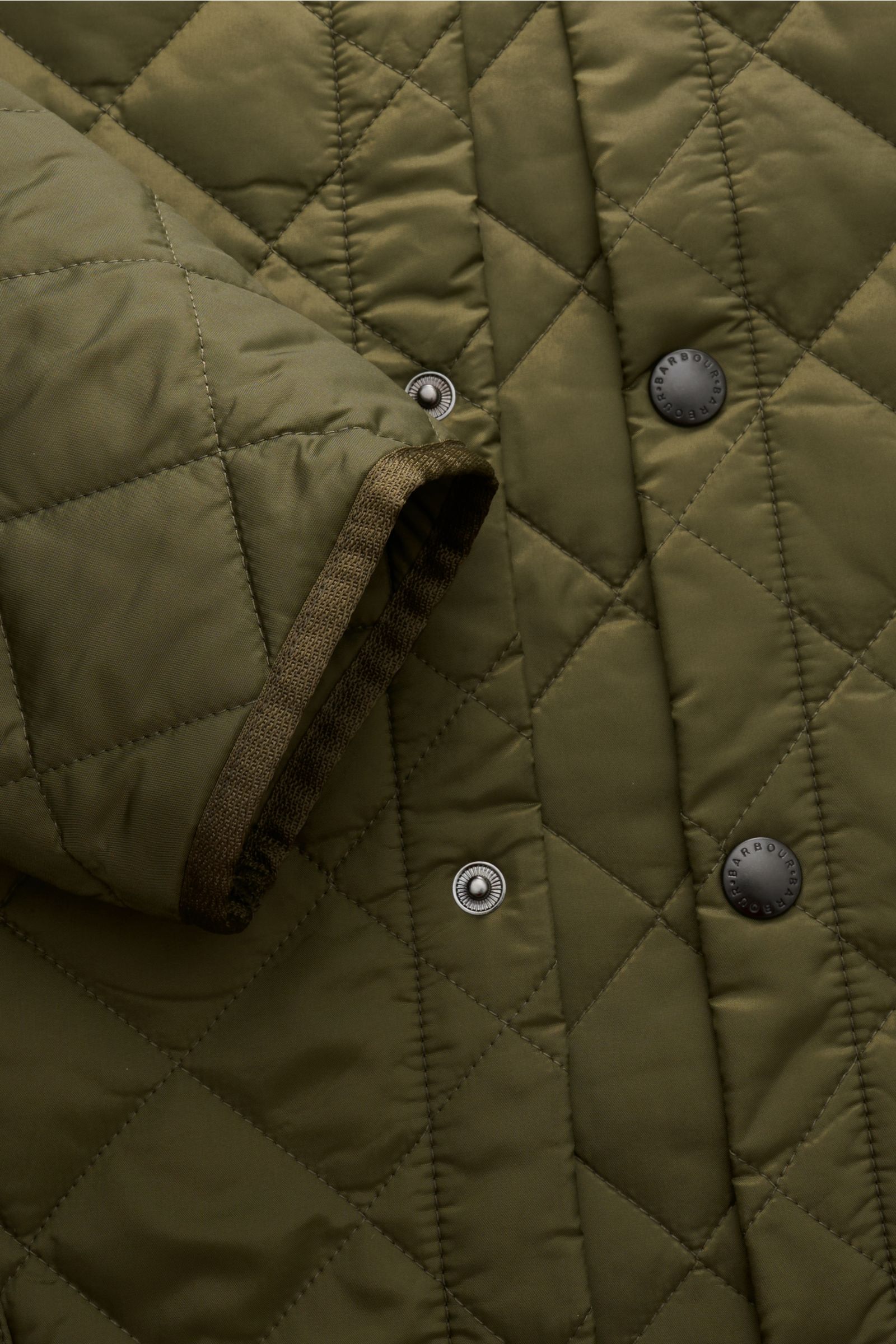 Nahaufnahme der olivfarbenen Barbour Steppjacke 'Liddesdale Quilt' mit leichter Wattierung, Druckknopfleiste, Saumschlitz und Cordbesatz am Ärmel.