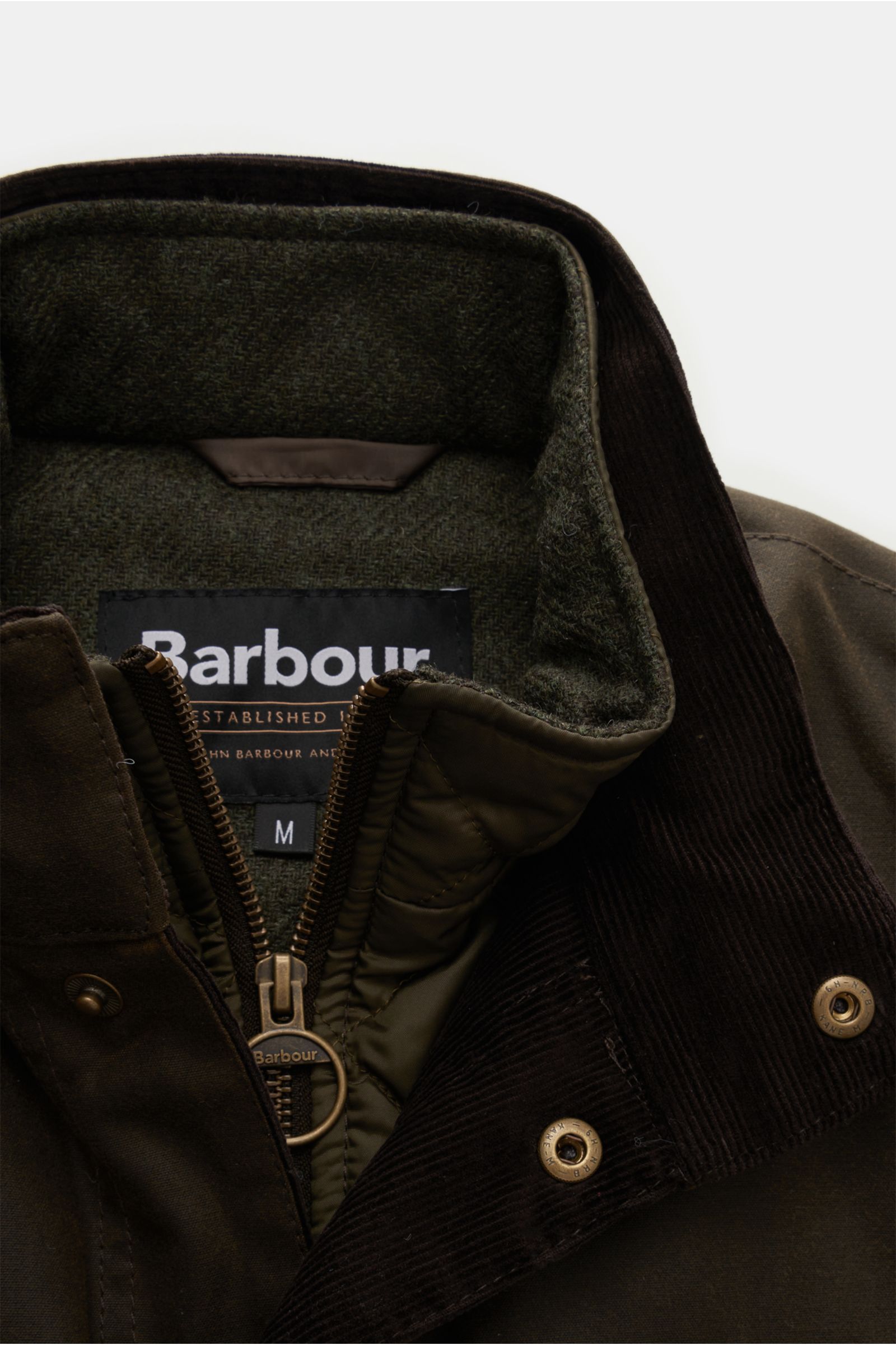 Close-up front view of Barbour Waxed jacket 'Ogston' dark olive, showing zip, snap button placket, standing collar, wool lining, and corduroy trim. Elegant, stylish, masculine: The modern waxed jacket 'Ogston' by BARBOUR in water repellent, waxed cotton w