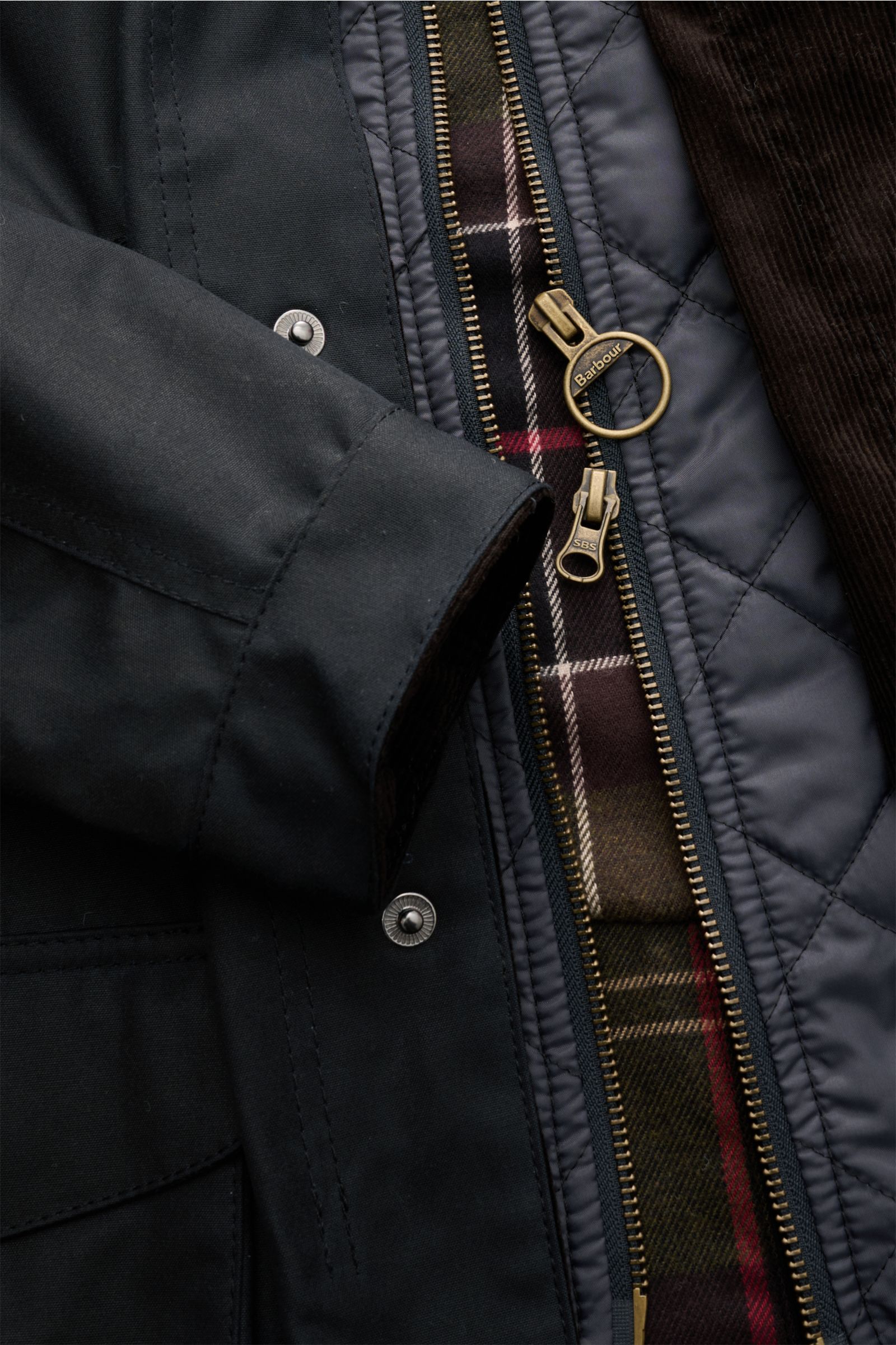 Nahaufnahme der Barbour Wachsjacke 'Ogston' dark navy von vorne mit geöffnetem Reißverschluss, gewachster Baumwolle, Tartan-Futter und Leder-Patches.