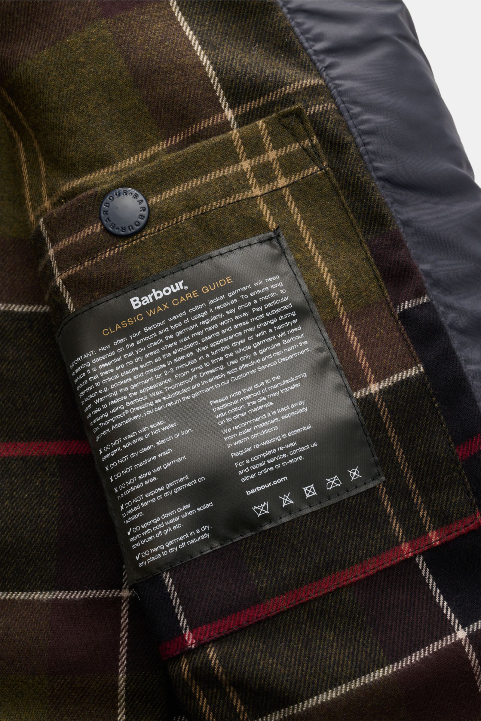 Nahaufnahme des charakteristischen Tartan-Futters der Barbour Wachsjacke 'Ogston' dark navy mit Pflegehinweis-Etikett und Druckknopf

Dieser Alt-Tag beschreibt aus der Perspektive einer Nahaufnahme das Innenfutter der Barbour Wachsjacke 'Ogston' dark na