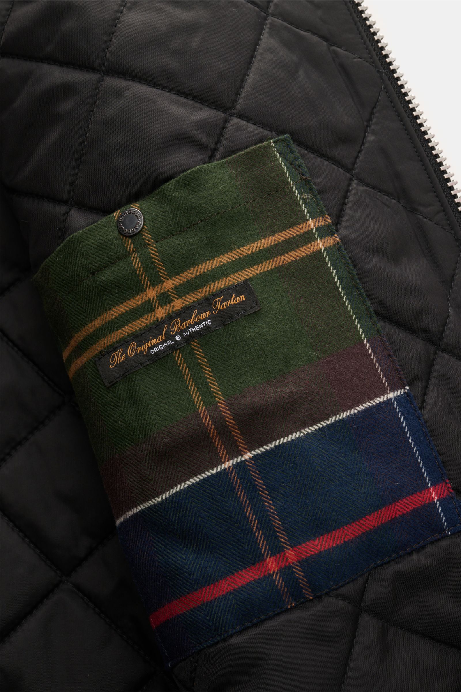 Nahaufnahme der leicht wattierten Innentasche der Barbour Wolljacke 'Bedale' anthrazit meliert mit griffigem Steppmuster und Tartan-Besatz.