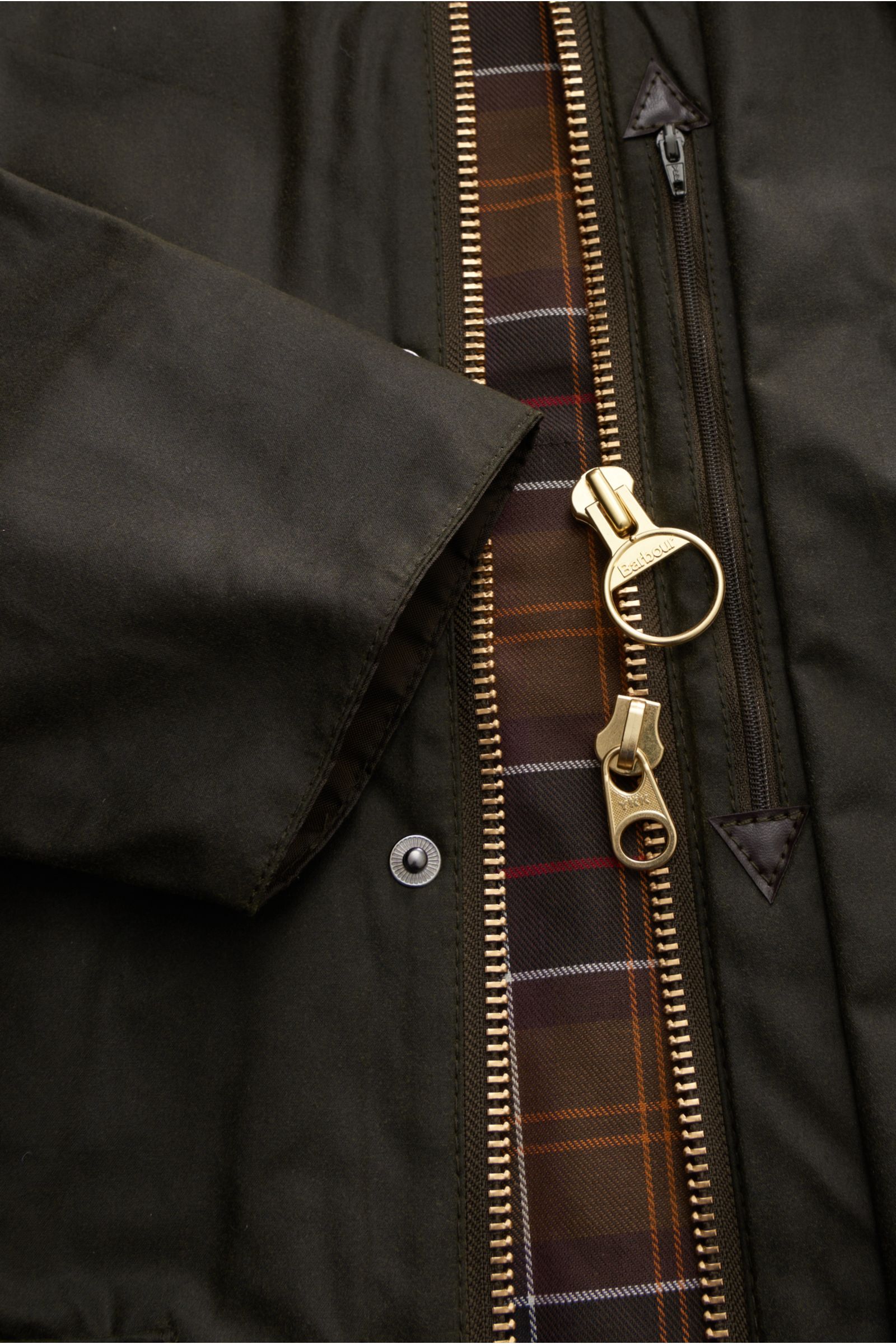 Close-up front view of Barbour Waxed jacket 'Beaufort' dark olive showing waxed cotton fabric, two-way zip, storm flap, and classic tartan lining.  
A true classic from BARBOUR: The long waxed jacket 'Beaufort' made of water repellent, waxed cotton wit