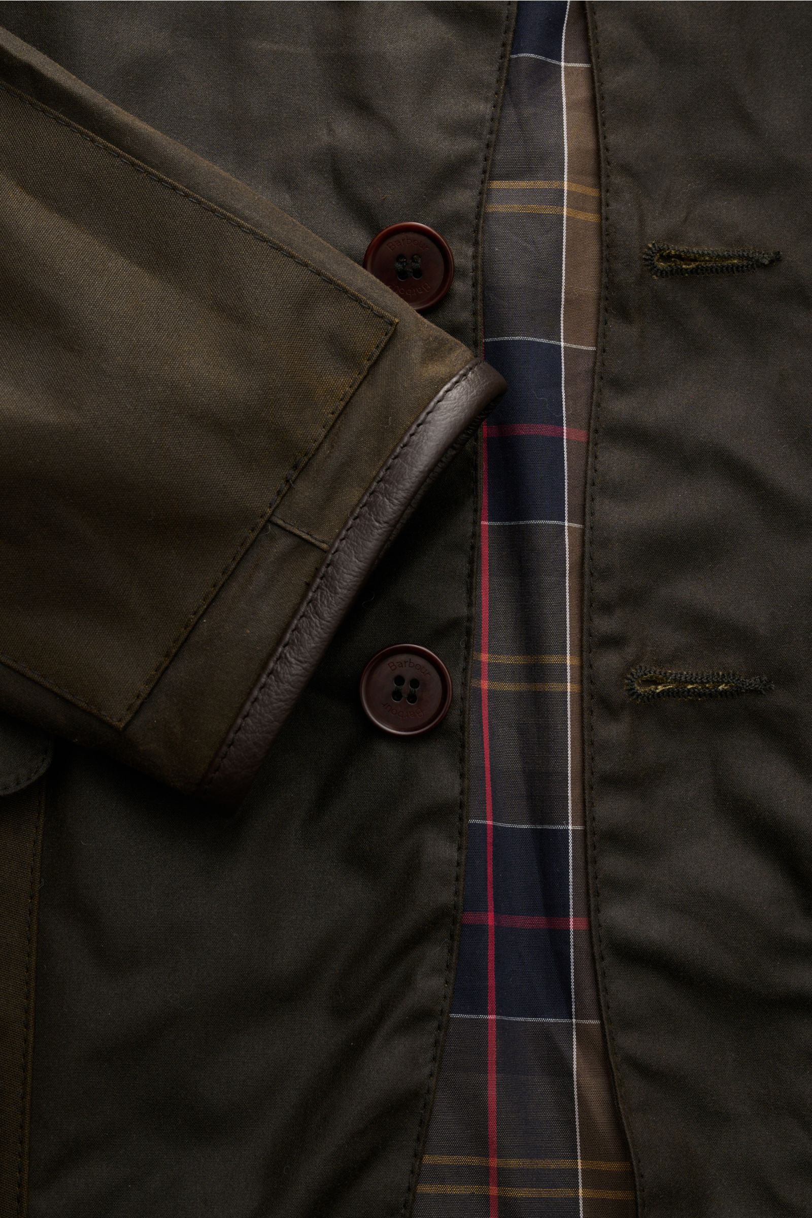 Barbour Wachsjacke 'Becan' dark olive, Detailaufnahme von Knopfleiste, gewachster Baumwolle, Lederbesatz am Ärmel und Tartan-Futter.