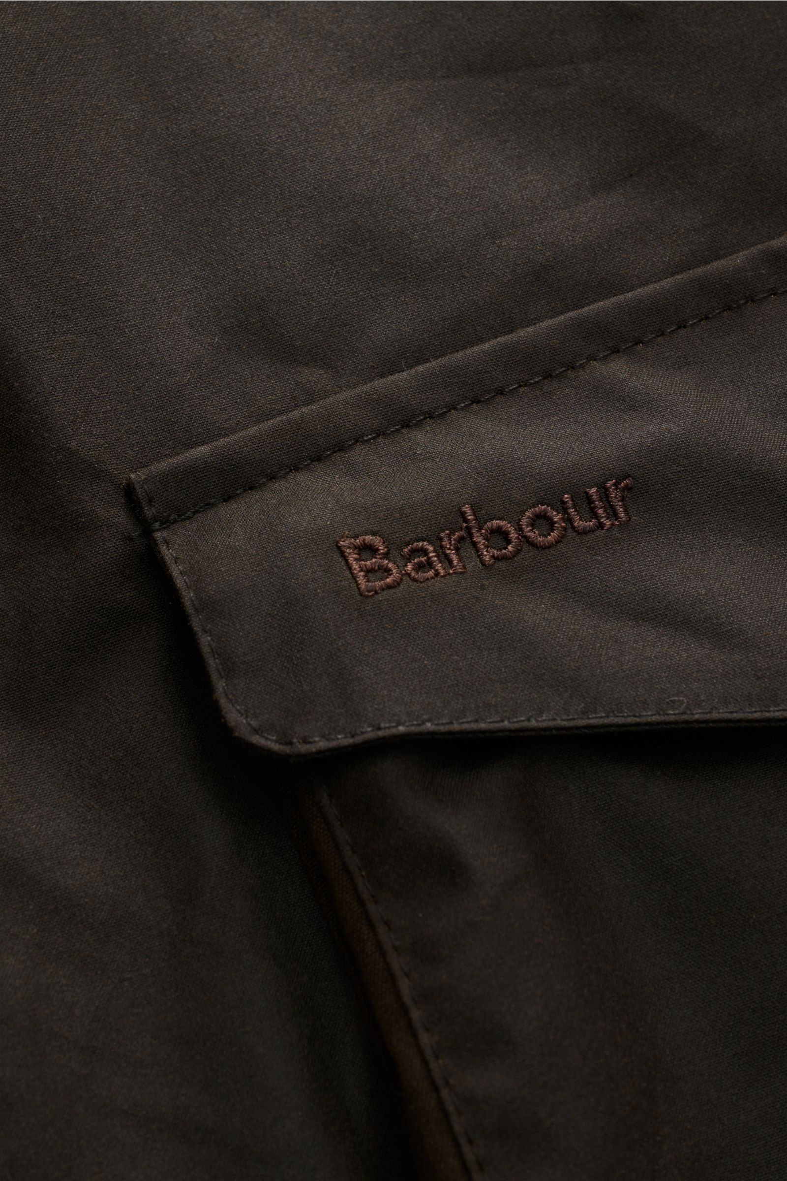 Nahaufnahme der aufgesetzten Brusttasche mit Label-Stitching der Barbour Wachsjacke 'Becan' dark olive aus gewachster Baumwolle.