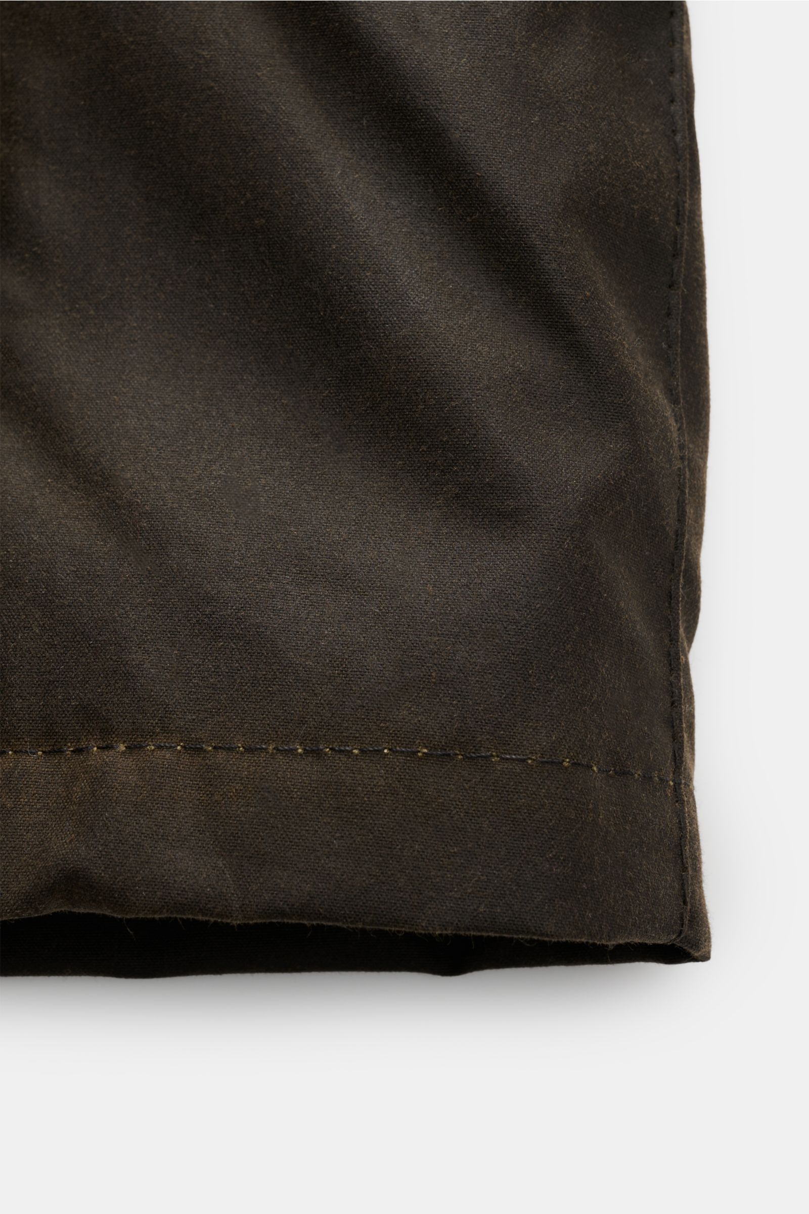 Nahaufnahme der wasserabweisenden Barbour Wachsjacke 'Becan' dark olive aus gewachster Baumwolle mit typischer Haptik, Detailansicht des Saums.