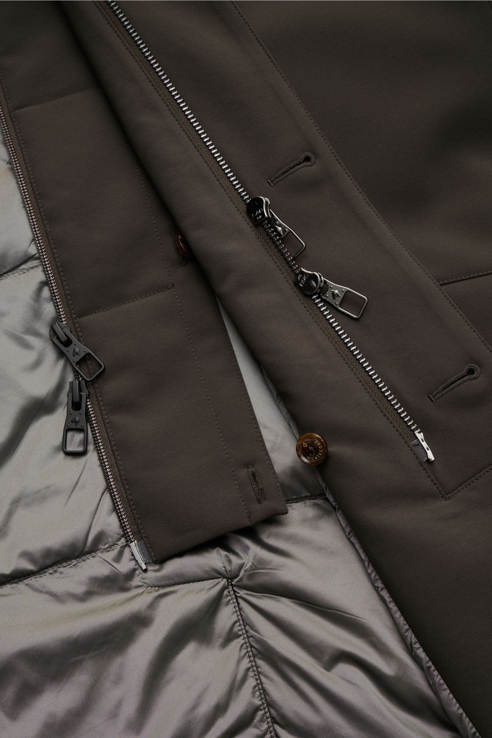 Nahaufnahme der geöffneten Montecore Daunenjacke dark olive, zeigt innen gestepptes, glattes Futter, AeroTwill-Material, zwei Reißverschlüsse, Knöpfe und Double-Front.