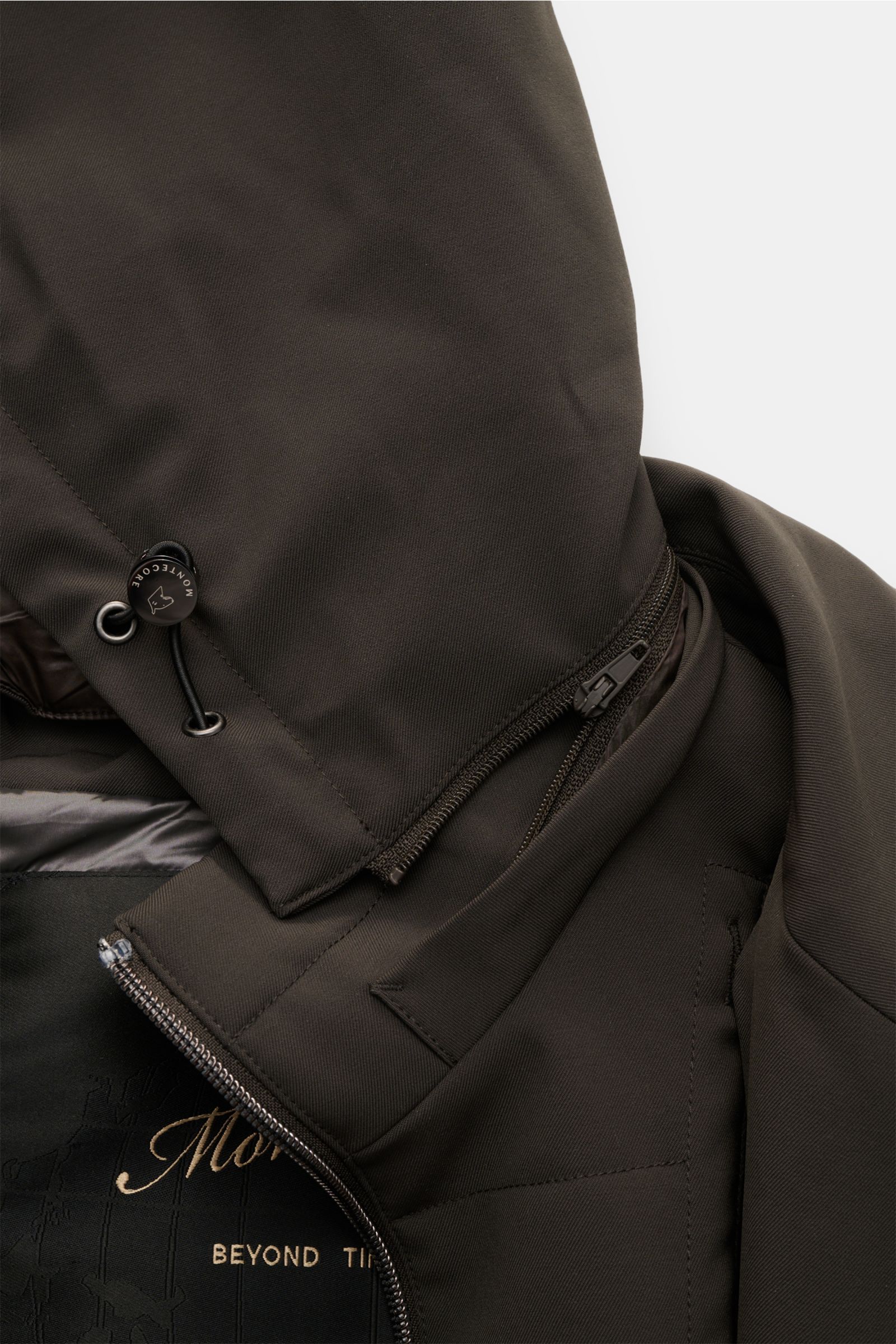 Montecore Daunenjacke dark olive in Nahaufnahme von oben, zeigt wind- und wasserabweisendes AeroTwill-Material, abnehmbare Kapuze mit Tunnelzug und Reißverschluss.