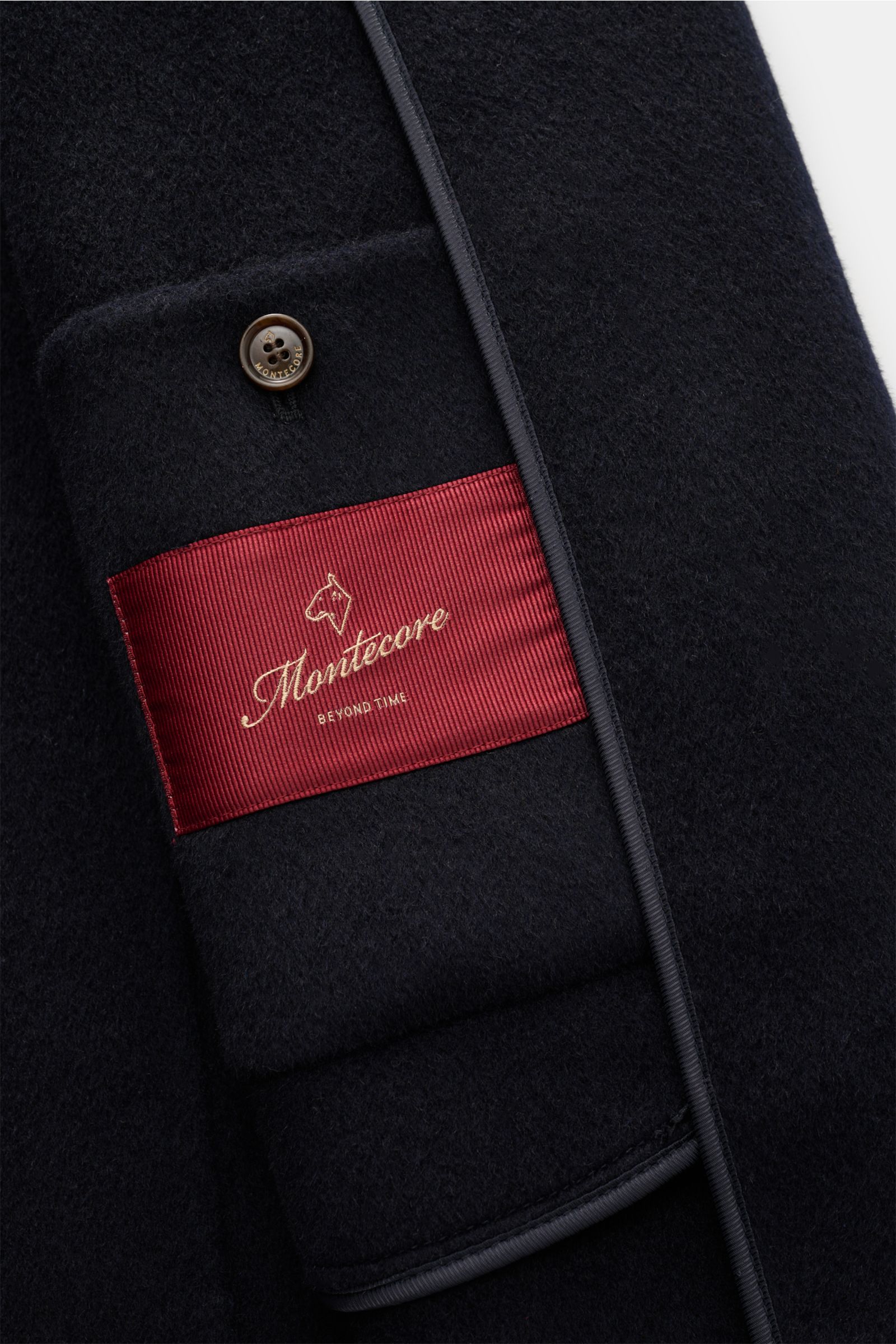 Close-up interior view of Montecore Cashmere Cabanjacke navy showing soft pure cashmere fabric, a button, and red Montecore label.