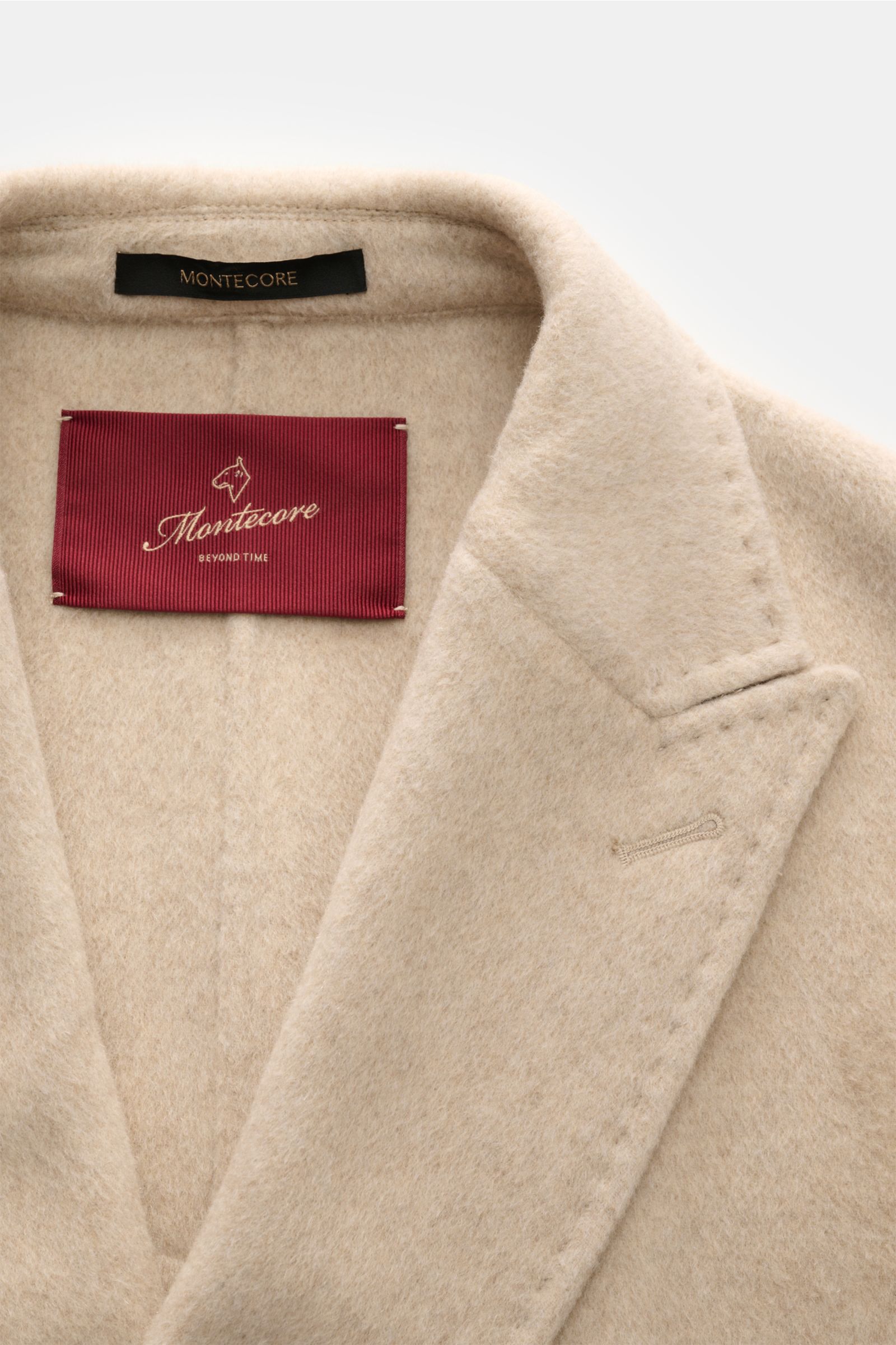 Nahaufnahme der Montecore Cashmere Cabanjacke beige von oben, zeigt das Spitzrevers, weichen Griff und das rote Markenlabel.
