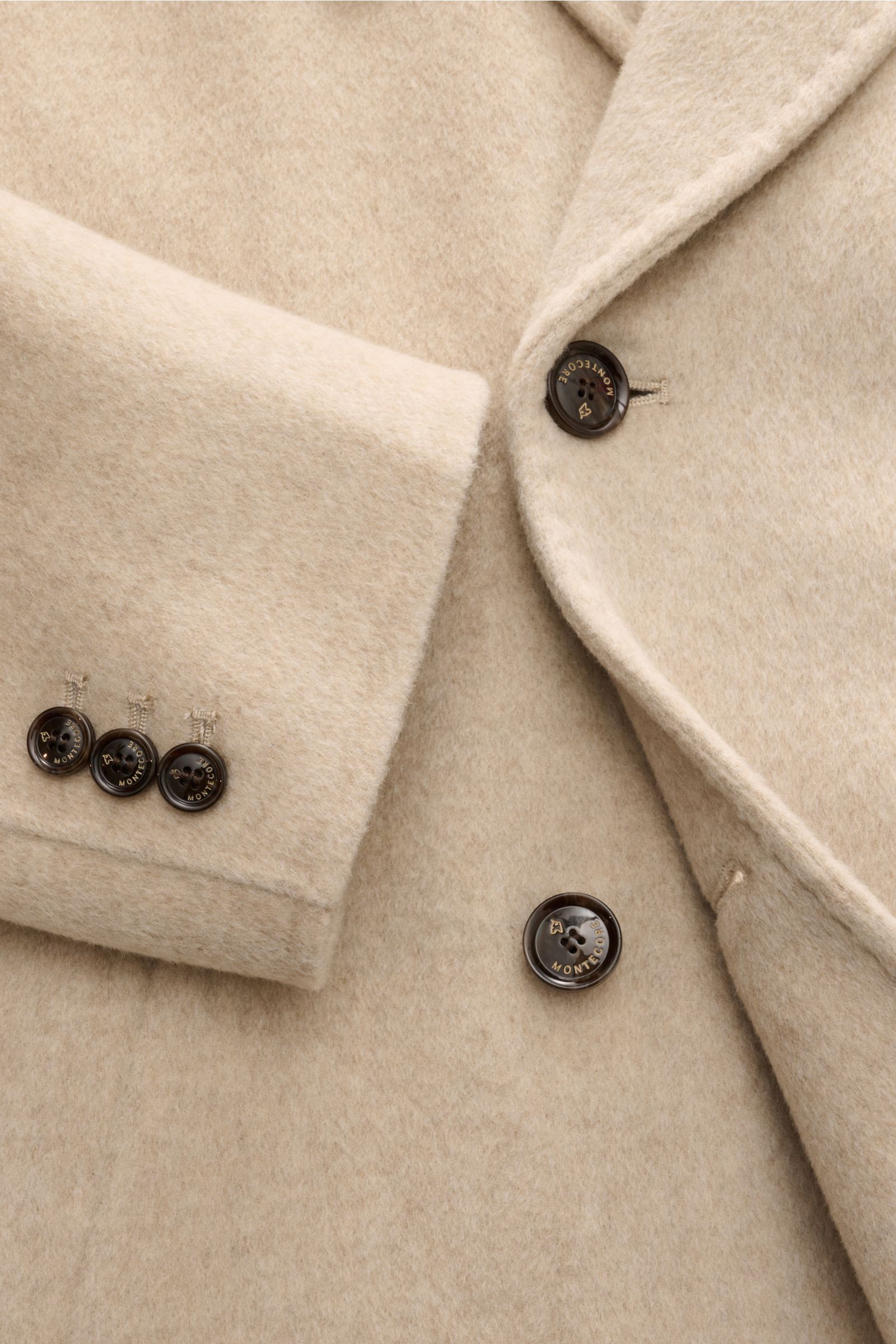Montecore Cashmere Cabanjacke beige in Nahaufnahme von oben, zeigt weichen Griff, Slim Fit, zweireihige Knöpfe, Spitzrevers und Ärmel mit drei Knöpfen.