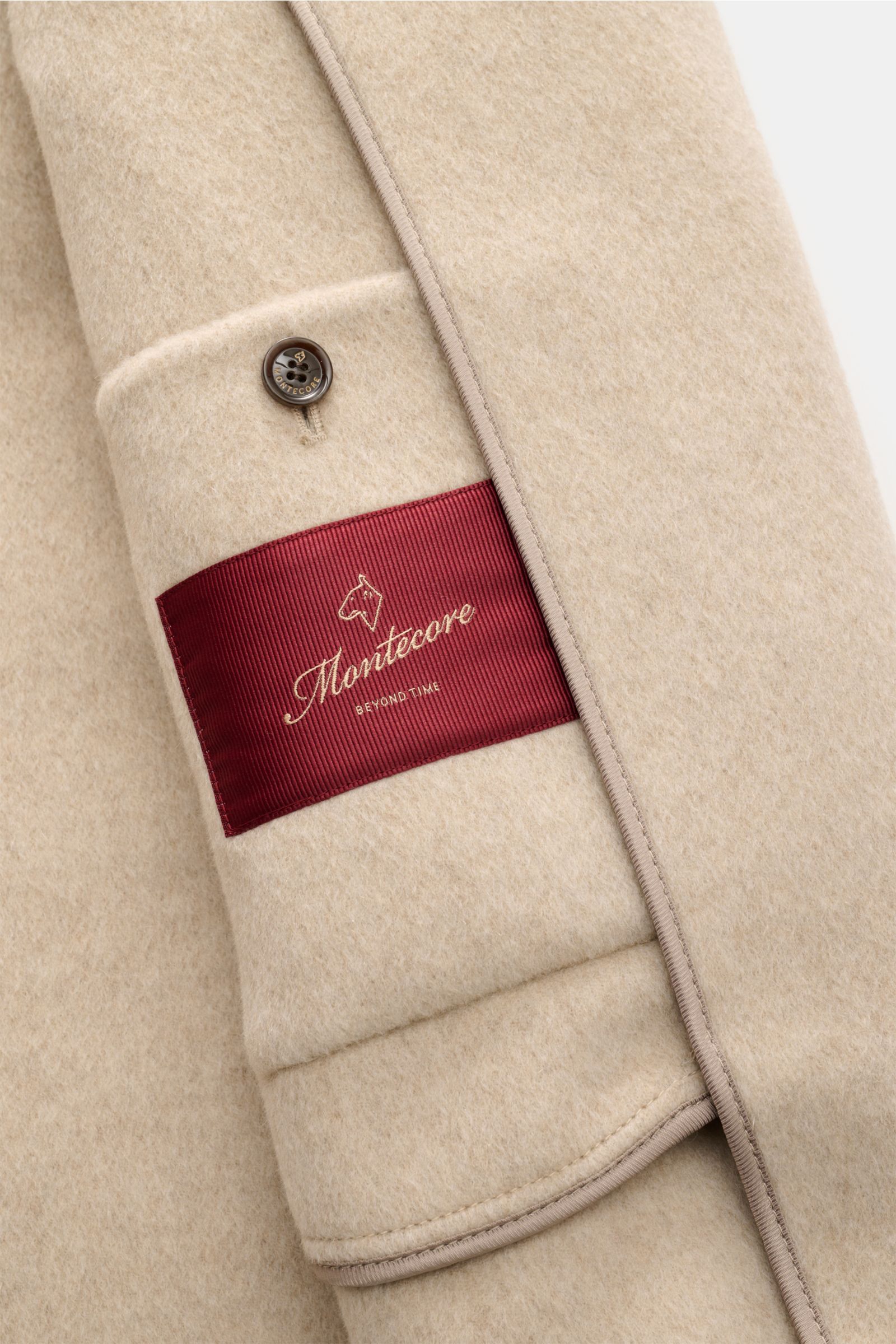 Montecore Cashmere Cabanjacke beige Nahaufnahme der Ärmelmanschette mit Knopf, rotem Logo-Etikett und weichem, reinem Cashmere.