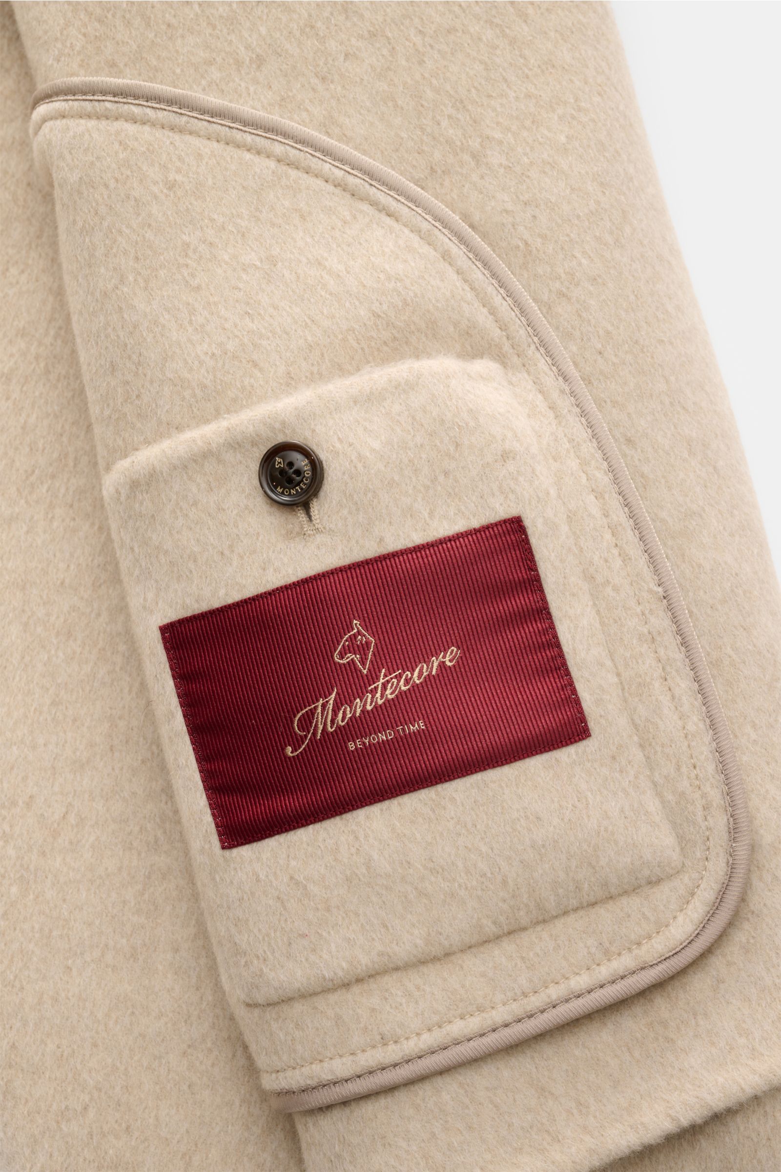 Nahaufnahme der Innentasche der Montecore Cashmere Jacke beige aus reinem Cashmere mit weichem Griff, Knopf und rotem Label, Detailfoto.