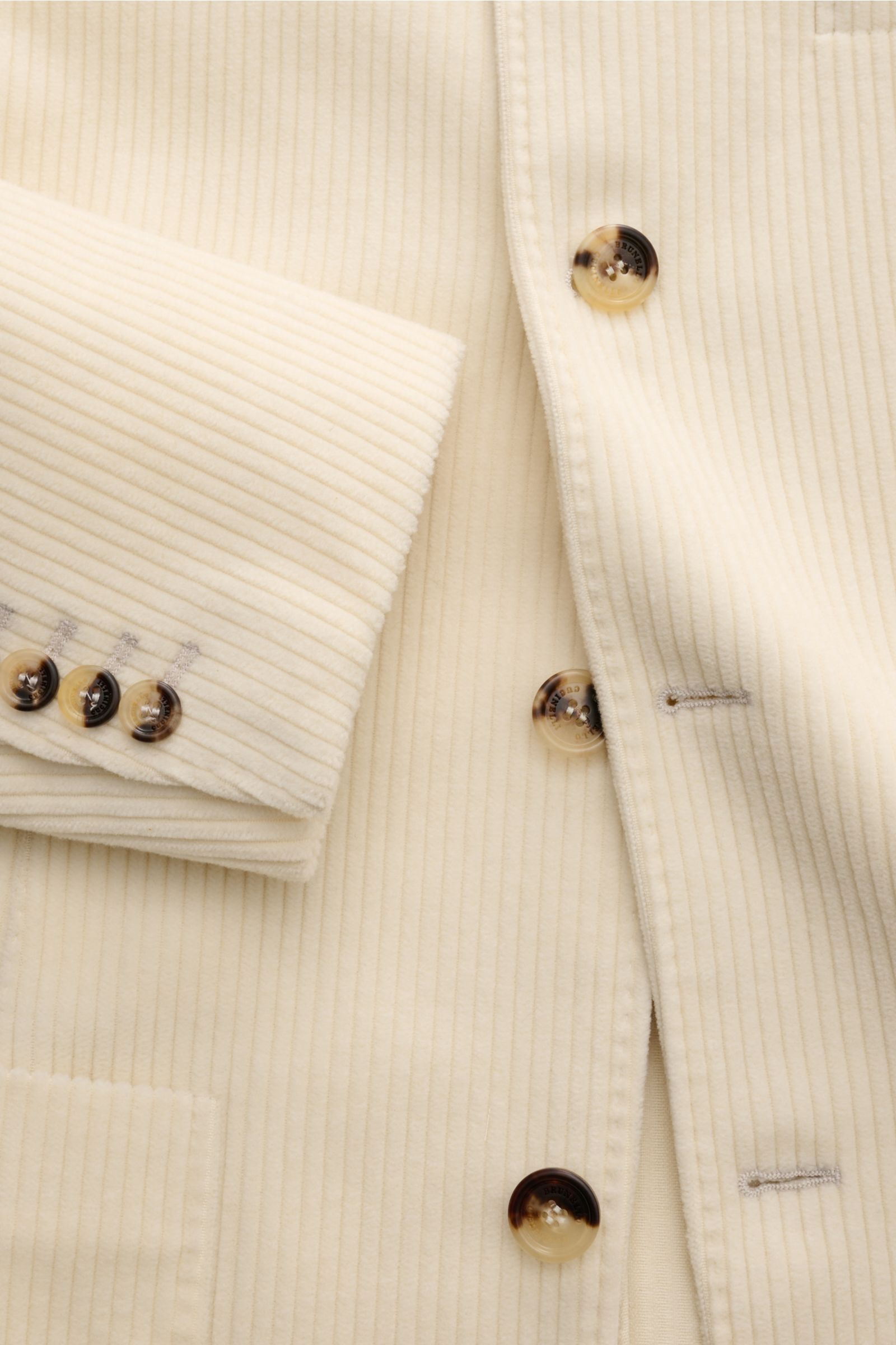 Close-up front view of Brunello Cucinelli Cashmere Cordjacke creme showing soft cream cord fabric, four-button slim fit, and cuff buttons.

Der zeitlose Stil dieser Cordjacke im Sakko-Design erhält von BRUNELLO CUCINELLI ein luxuriöses Upgrade durch di