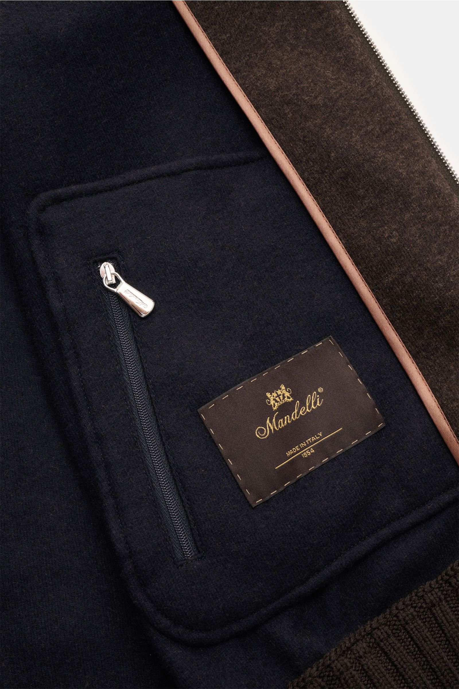 Close-up inside view of the Mandelli Jersey-Blouson dunkelbraun showing a zippered inner pocket, brand label, and soft fabric details.

Description: Luxus und Komfort gehen mit diesem ungefütterten Jersey-Blouson aus dem Hause MANDELLI eine Fusion ein.