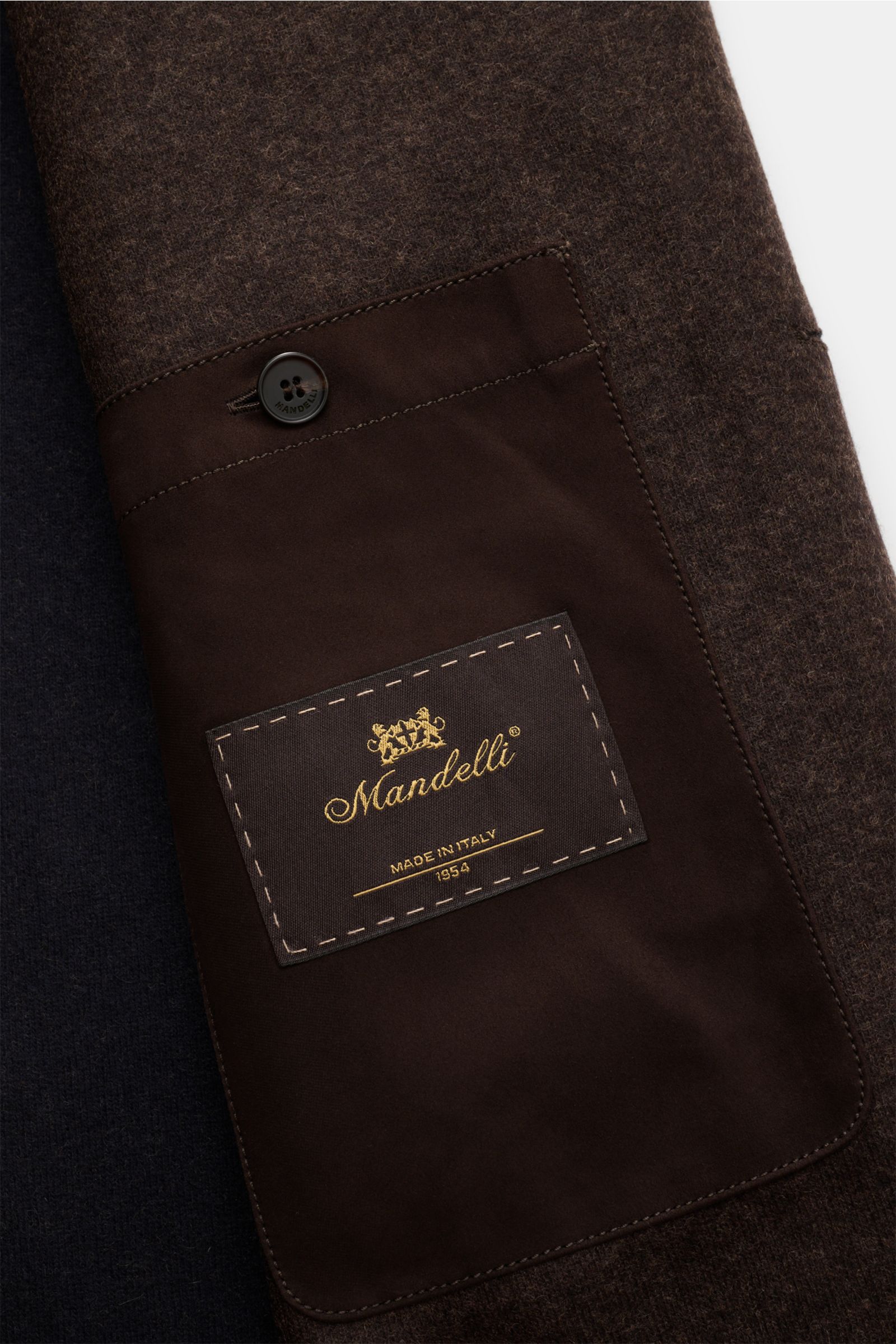 Nahaufnahme der Innentasche der Mandelli Cashmere Jacke dunkelbraun meliert mit Knopf und Markenlabel, zeigt feinen Jersey und weiche Haptik.