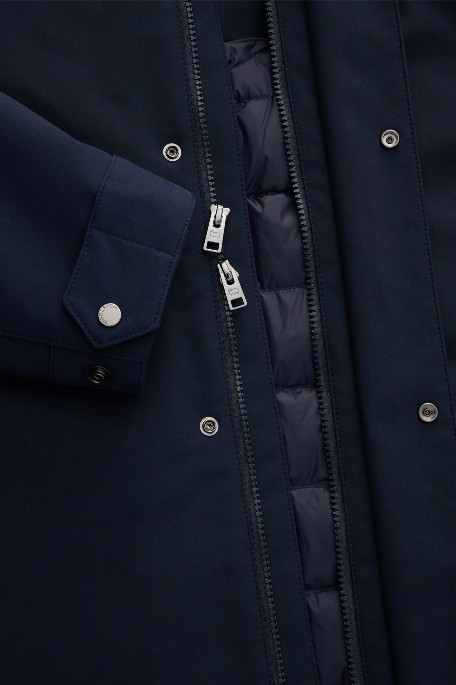 Close-up front view of the Woolrich Softshell-Daunenparka schwarz showing the elastic microfiber softshell fabric, smooth surface, water-repellent finish, warm down filling, robust two-way zipper, snap buttons on the cuff, and quilted inner lining. Der