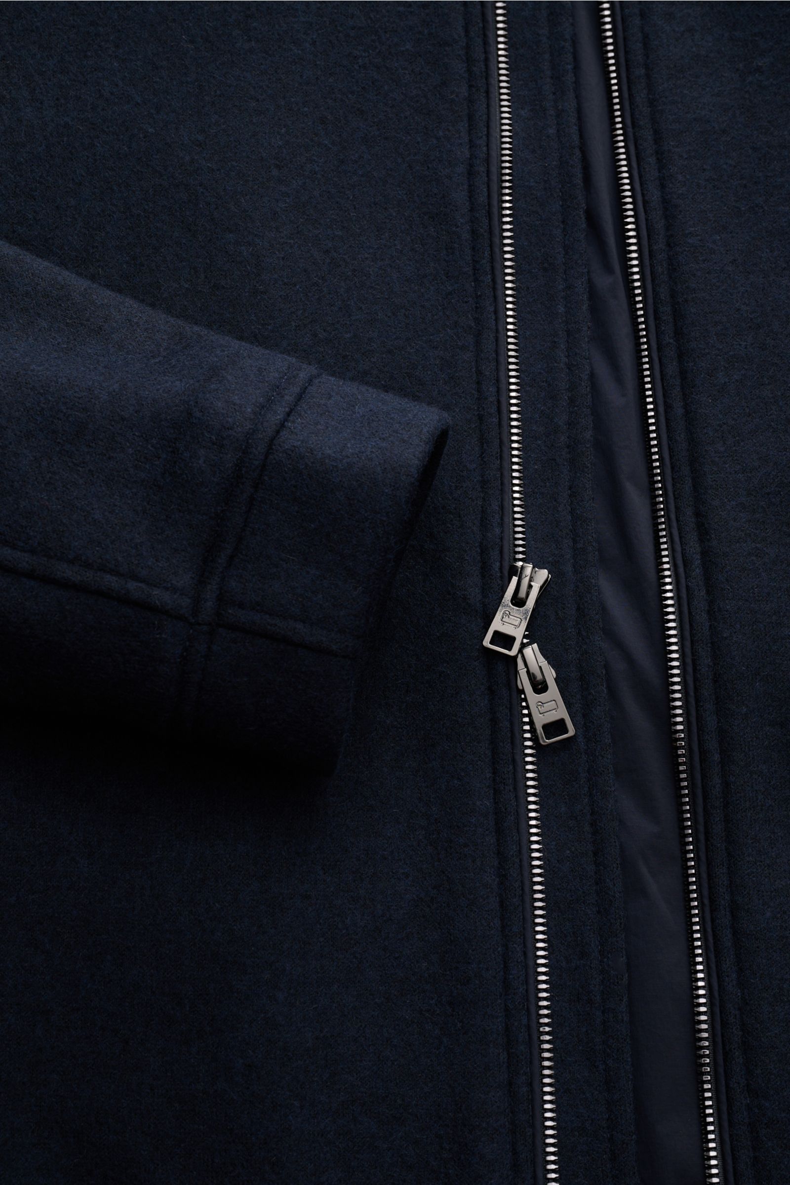 Nahaufnahme der Woolrich Daunenjacke navy, aus Wolle und Microfaser mit Slim Fit, Druckknopfleiste, variablen Kragen, Leistentaschen, Knopfärmeln, regulierbarer Taille, gesteppter Innenfutter und zwei Innentaschen, seitlich fotografiert.