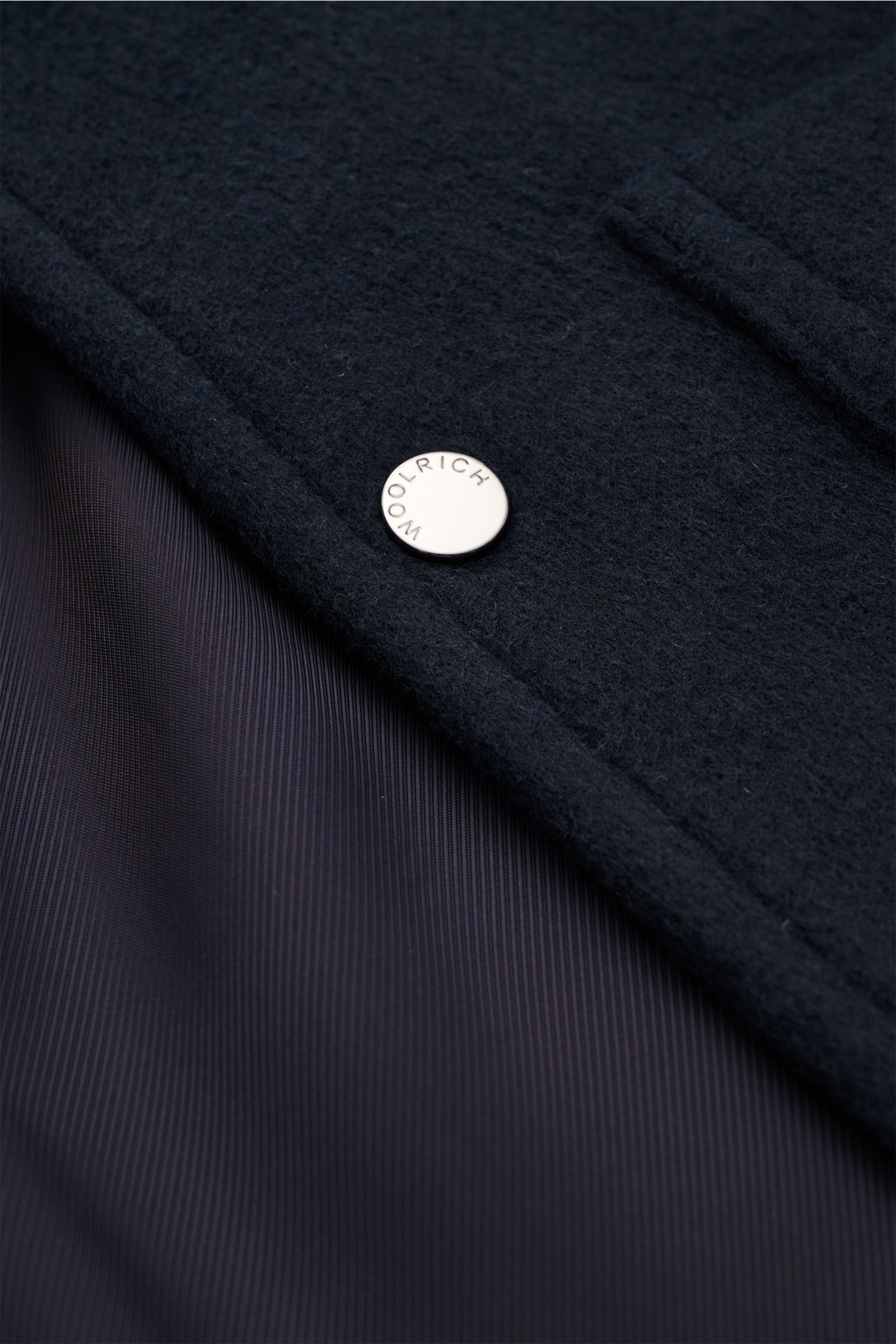 Close-up front view of the Woolrich Jacke 'Chore' navy showing the soft wool-mix fabric, metal WOOLRICH snap button, and smooth lining. Zeitlose Eleganz vom Jacken-Experten WOOLRICH: Das leichte Modell 'Chore' aus softem Woll-Mix wird zum idealen Layer