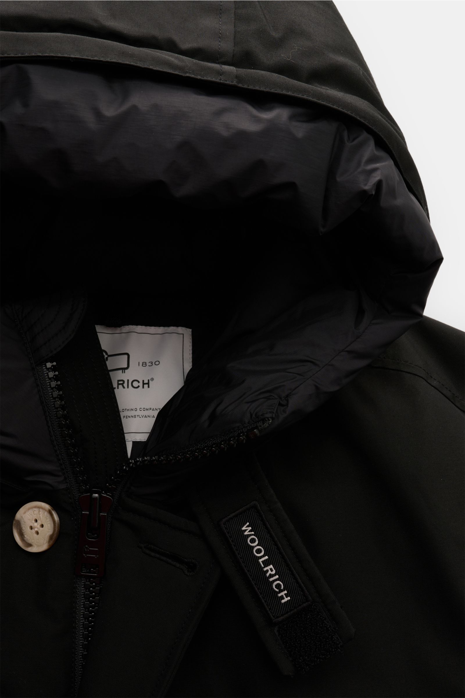 Close-up front view of the Woolrich Daunenparka 'Arctic Parka' schwarz showing the hood interior, zipper, button, and collar with Woolrich label, featuring cotton and microfiber mix, warm down filling, slim fit, two-way zipper, wind flap with buttons, dow