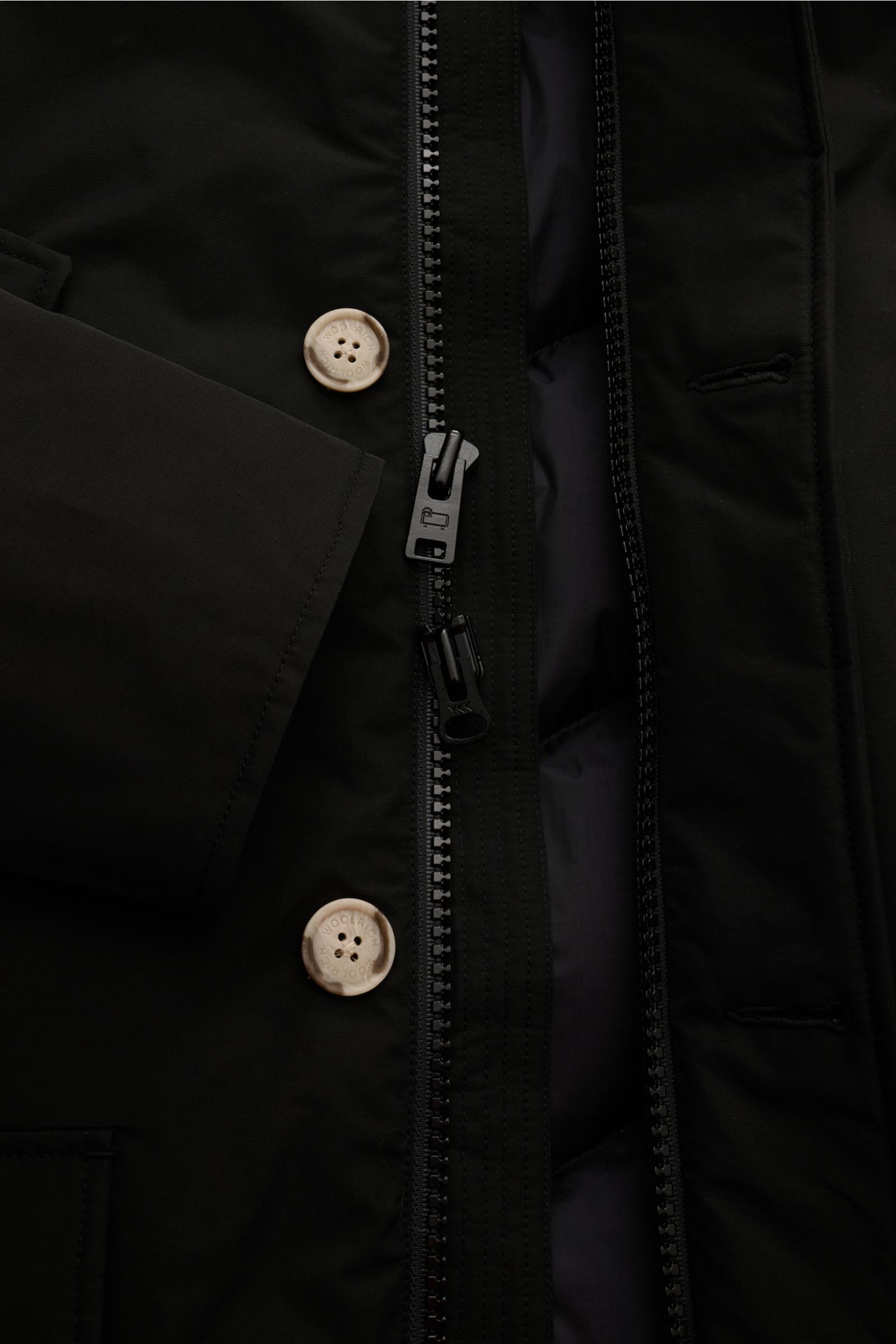 Close-up front view of Woolrich Daunenparka 'Arctic Parka' schwarz showing black cotton-microfiber fabric, two-way zipper, and branded buttons. Kälte? Kann kommen. Der 'Arctic Parka' von WOOLRICH liefert sportiven Style und verlässliche Wärme bis –20 °C –