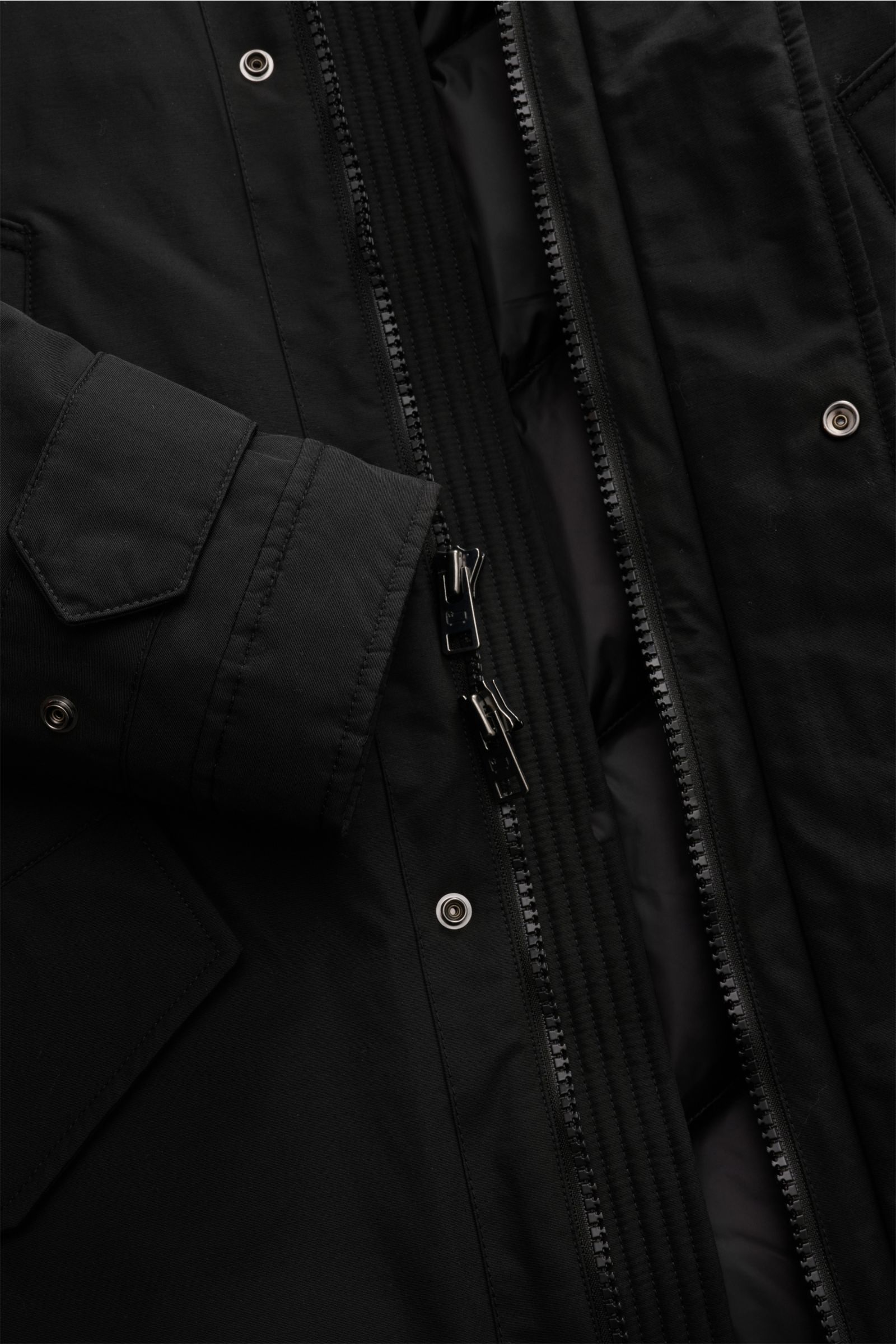 Nahaufnahme des schwarzen Woolrich Daunenparkas 'Polar High Collar' von innen mit robustem Zwei-Wege-Reißverschluss, wattierter Kapuze, wind- und wasserabweisendem Ramar Cloth Gewebe, Slim Fit und verstellbaren Ärmelabschlüssen.