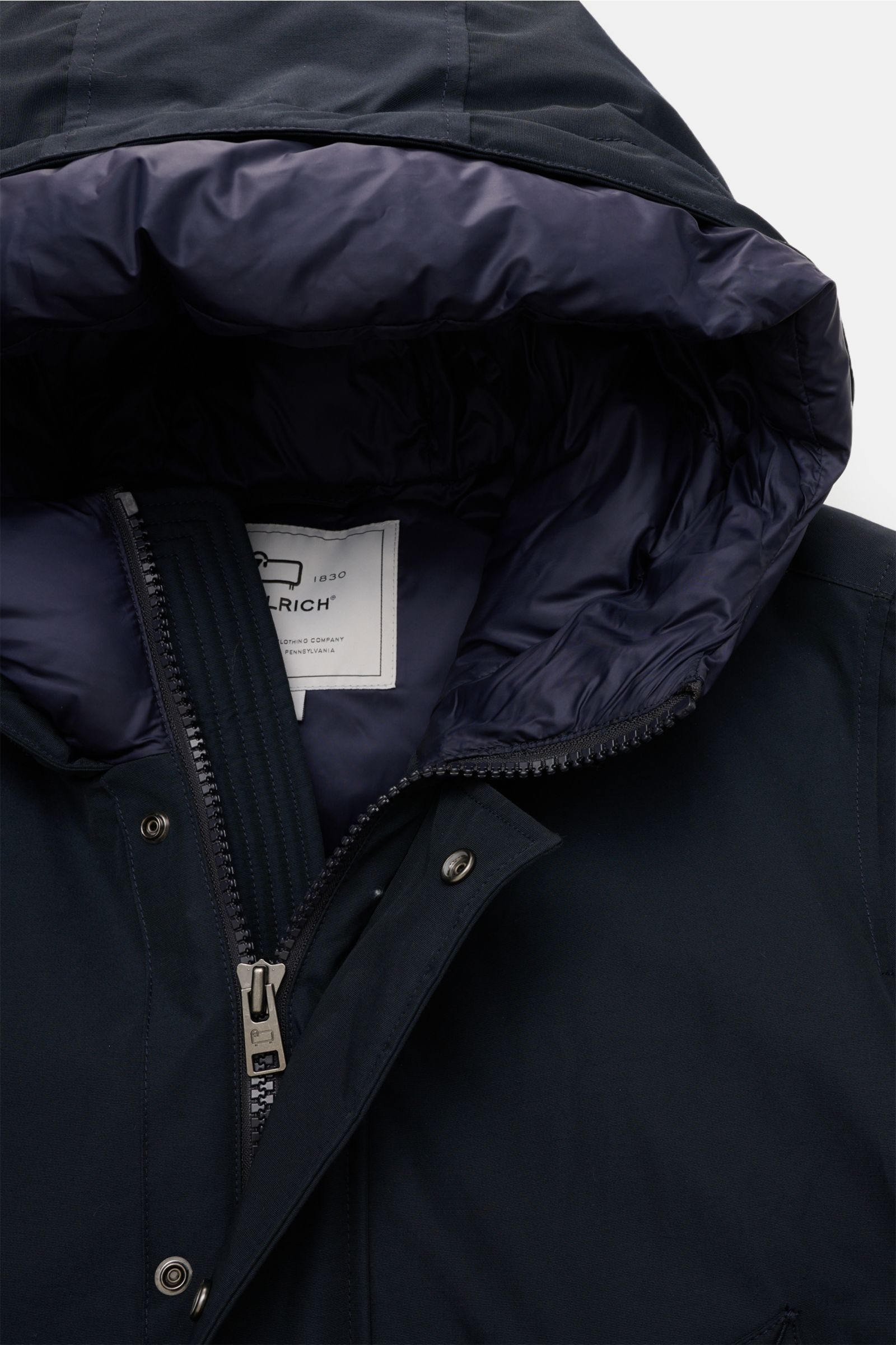 Nahaufnahme aus schräger Perspektive des Woolrich Daunenparka 'Polar High Collar' navy mit wattierter Kapuze, robustem Zwei-Wege-Reißverschluss und wind- sowie wasserabweisendem Ramar Cloth Gewebe.