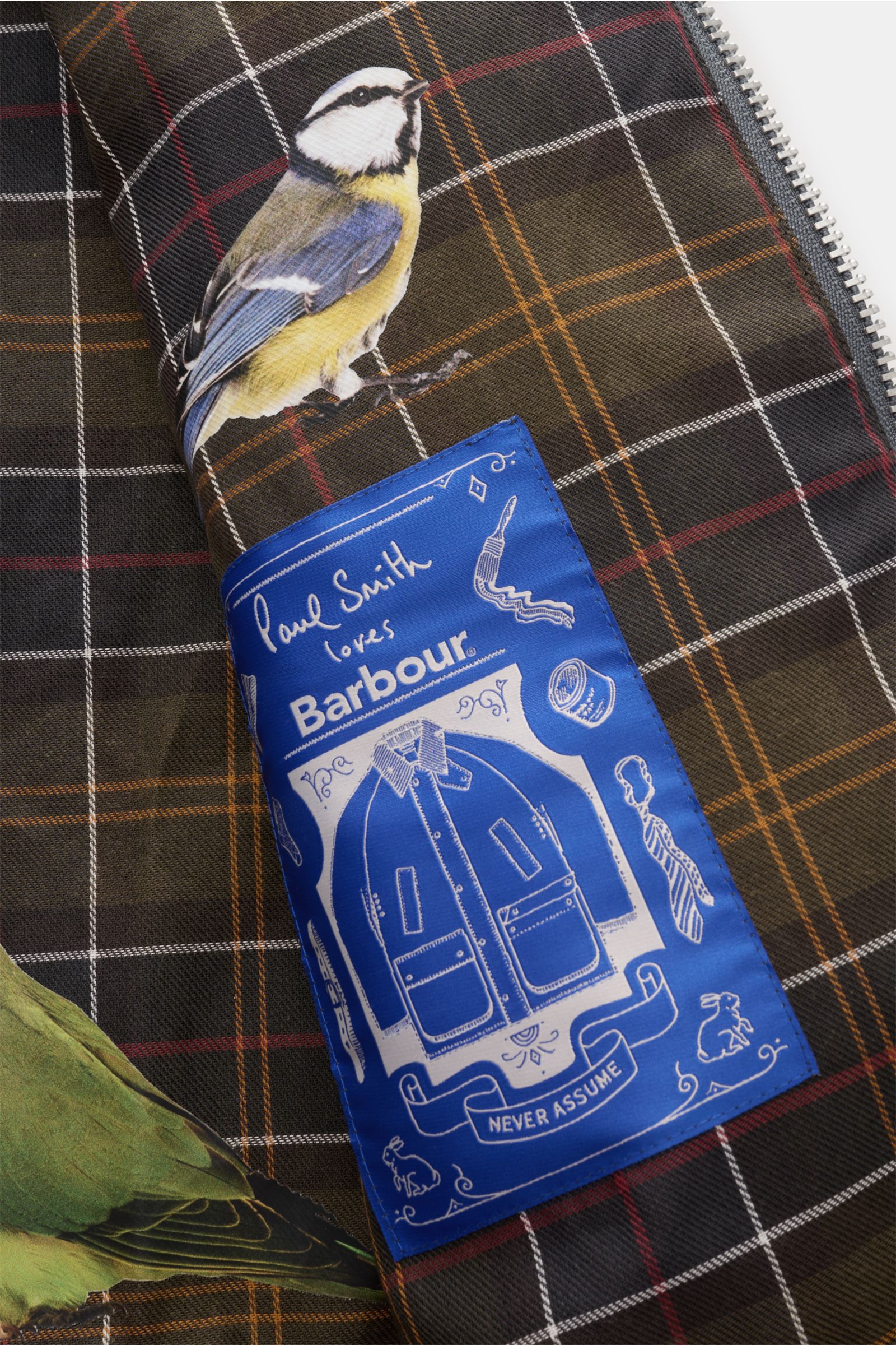Nahaufnahme des Tartan-Innenfutters der Barbour Wachsjacke 'Transport' petrol mit Vogel-Prints und Paul Smith x Barbour Label.