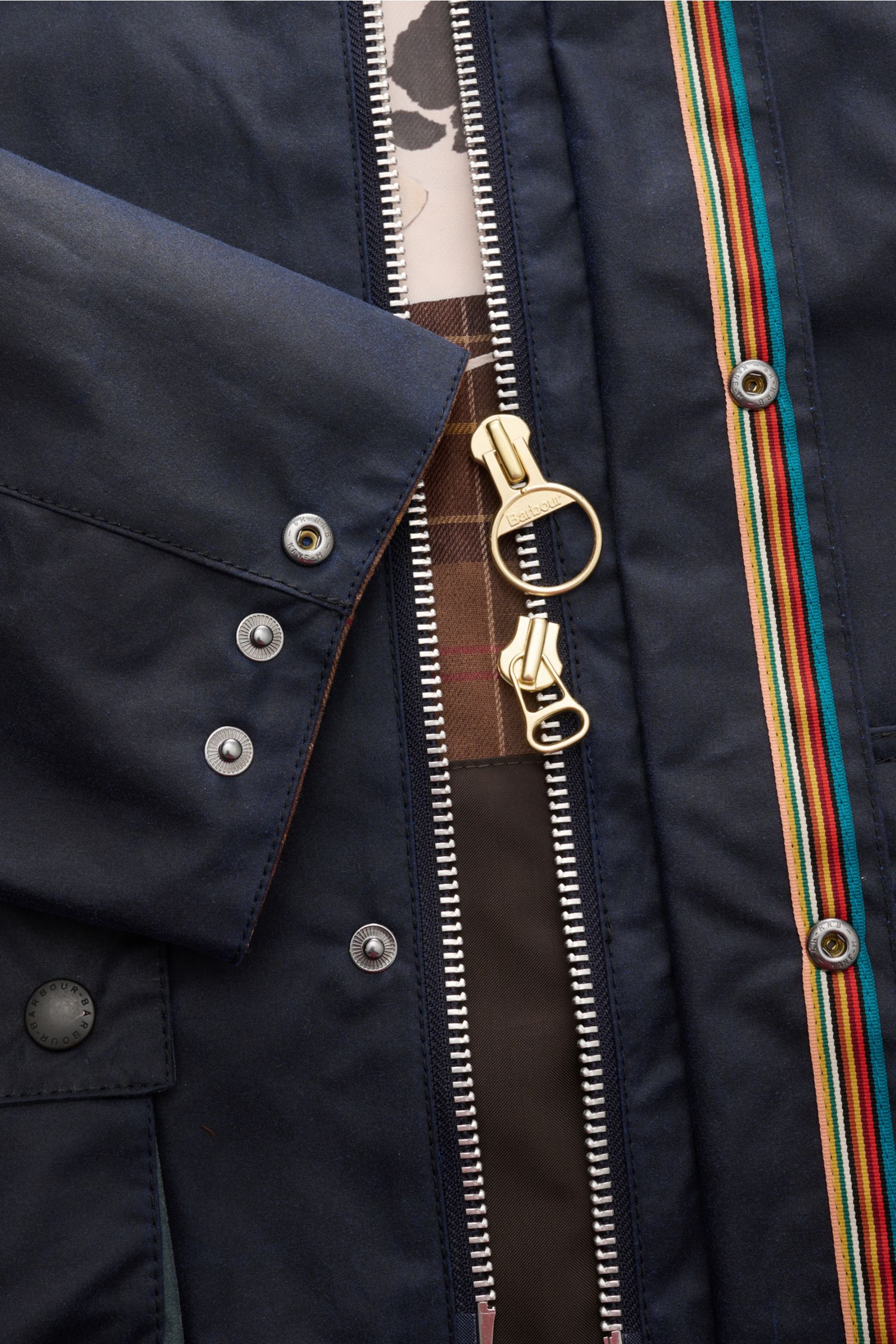 Barbour Wachsjacke 'Bedale' navy aus gewachster Baumwolle, Detailaufnahme von Reißverschluss, Druckknöpfen und Tartan-Futter mit Kuh-Print.