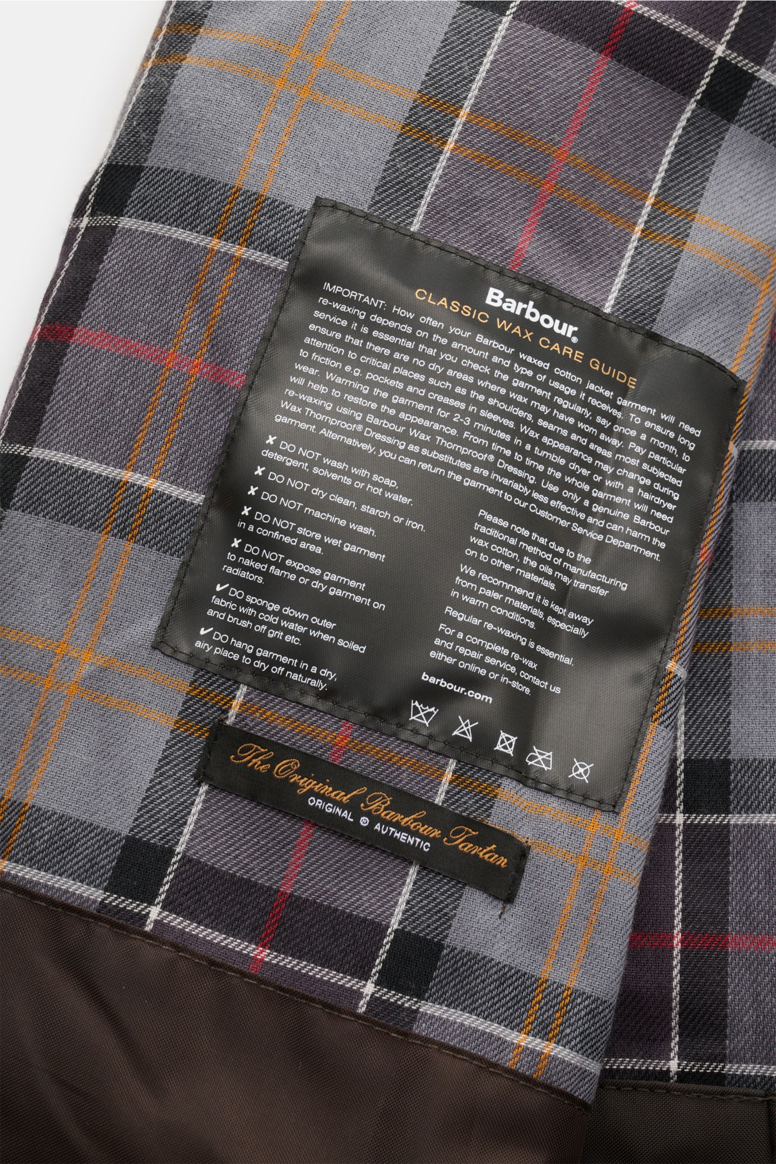 Nahaufnahme des Tartan-Innenfutters mit Pflegehinweisen der Barbour Wachsjacke 'Bedale' braun, Kooperationsmodell mit Paul Smith.