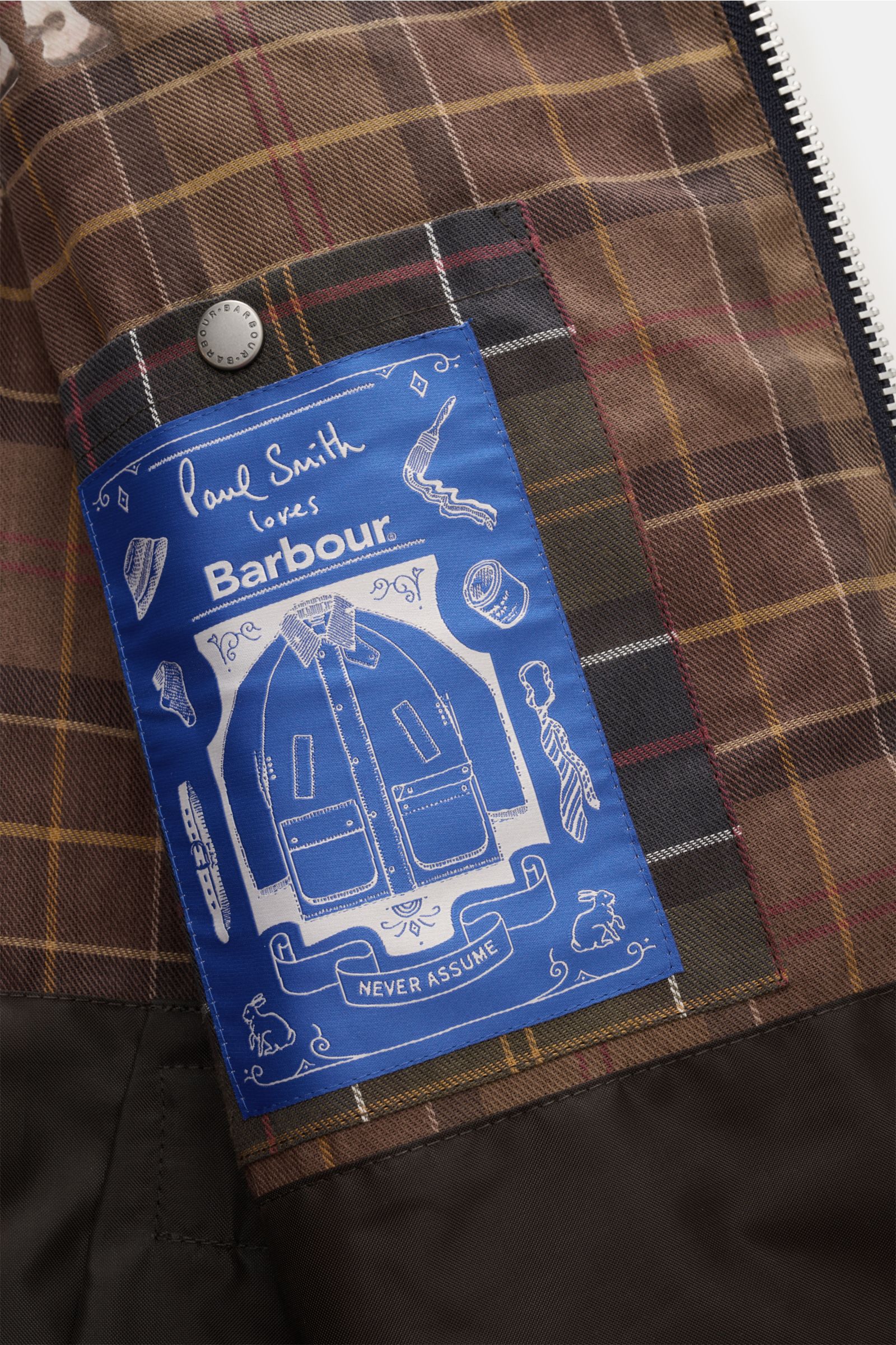 Close-up inside view of the Barbour Wachsjacke 'Bedale' navy/bordeaux/petrol showing the brown tartan lining with a blue Paul Smith loves Barbour label and silver snap button.

Gut gerüstet für die Übergangszeit: Diese Variante der 'Bedale' Jacke gehör