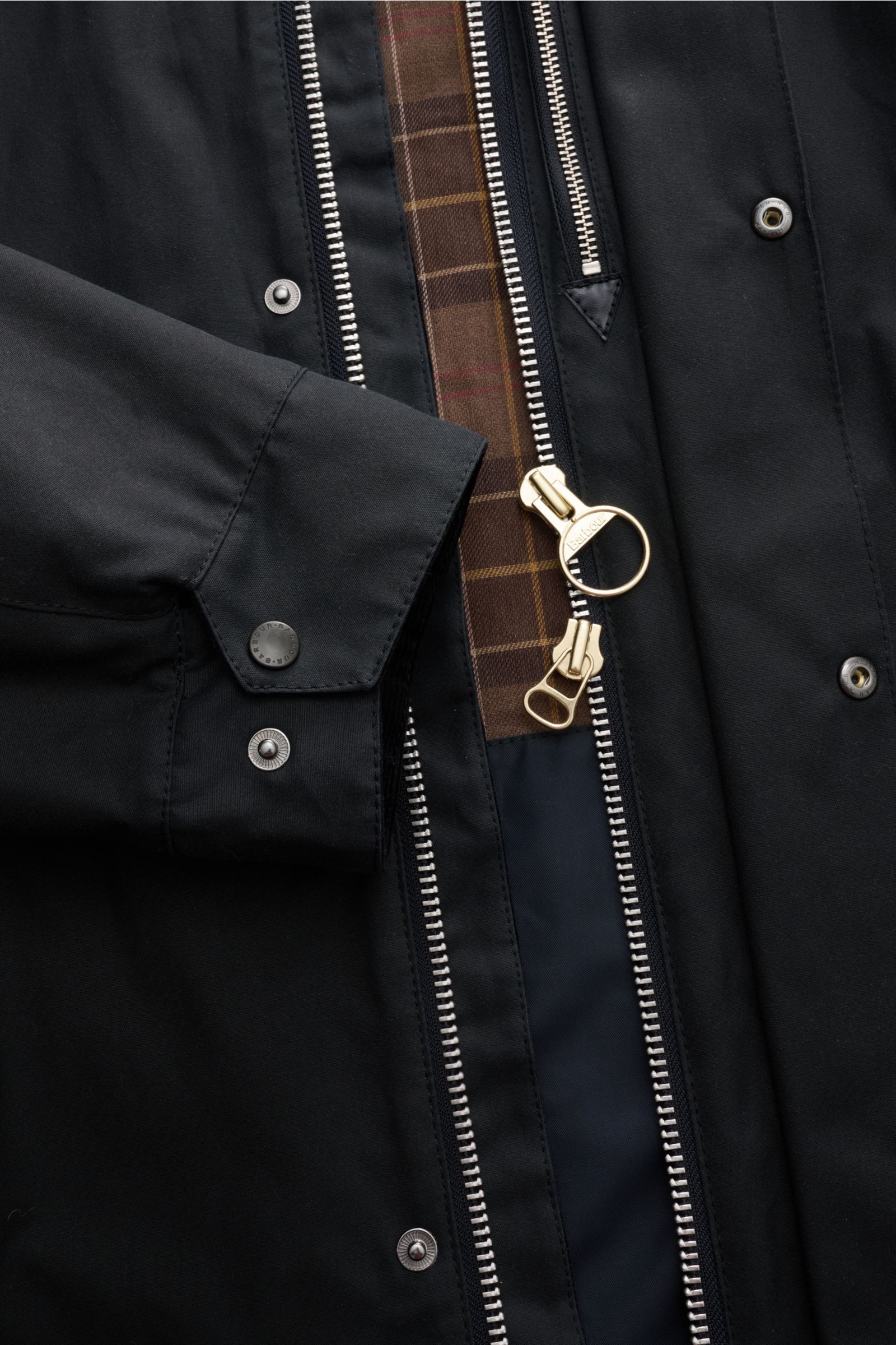 Close-up front view of the Barbour Wachsparka 'Beeston' navy showing waxed cotton fabric, slim fit sleeve cuff with snap buttons, robust two-way zipper with Barbour ring pull, and typical tartan lining. Gut gerüstet für die Übergangszeit: Der 'Beeston' Wa