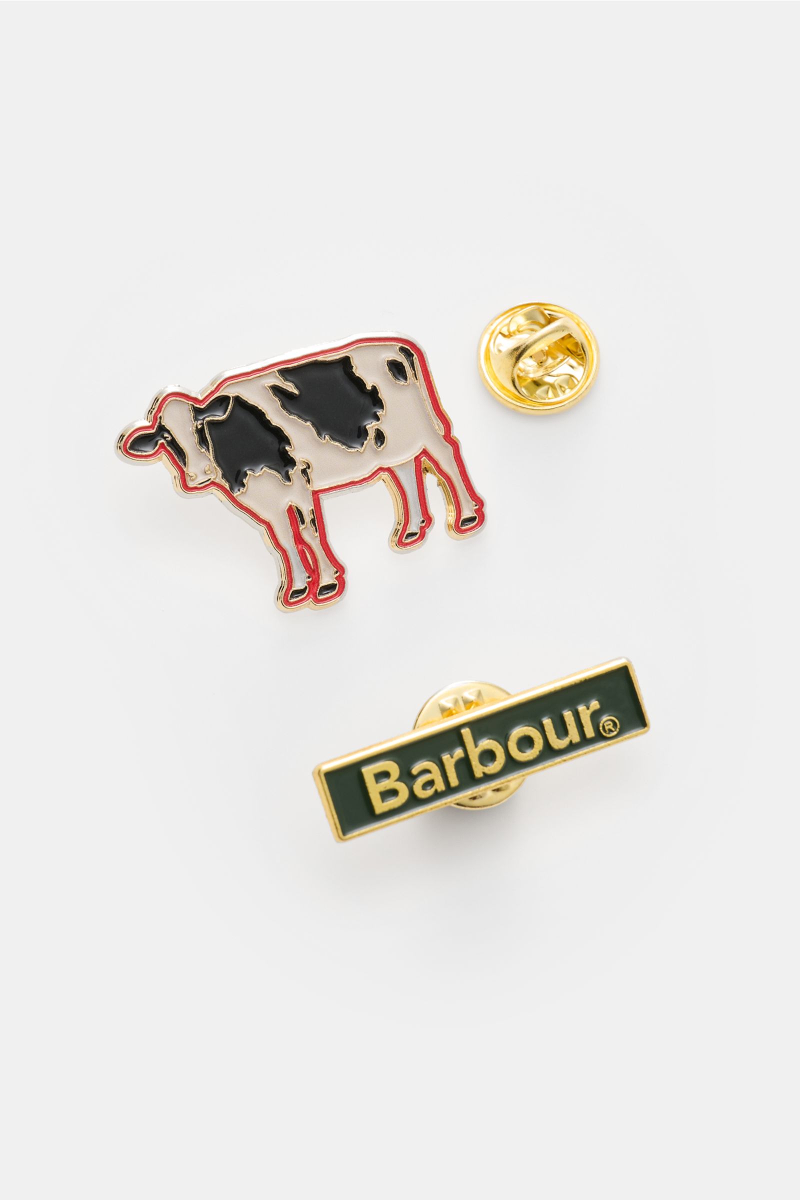 Pin set shown from a top-down view, featuring a cow-shaped enamel pin with black and white patches outlined in red, and a rectangular green and gold 'Barbour' logo pin. The pins complement the Barbour Wachsparka 'Beeston' navy, a waxed cotton slim-fit par